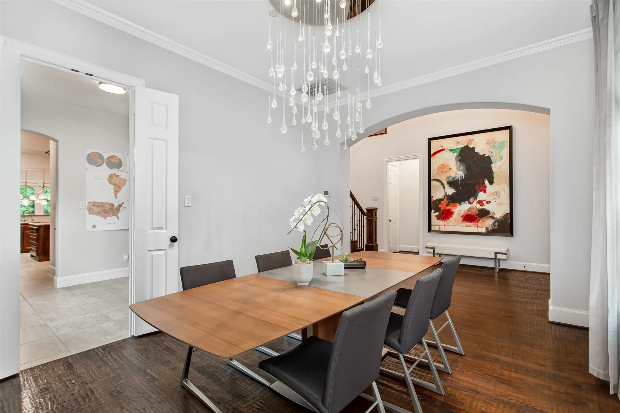 Formal dining area featuring dark wood-finish flooring, a modern drop crystal chandelier, and a wide arched entryway
