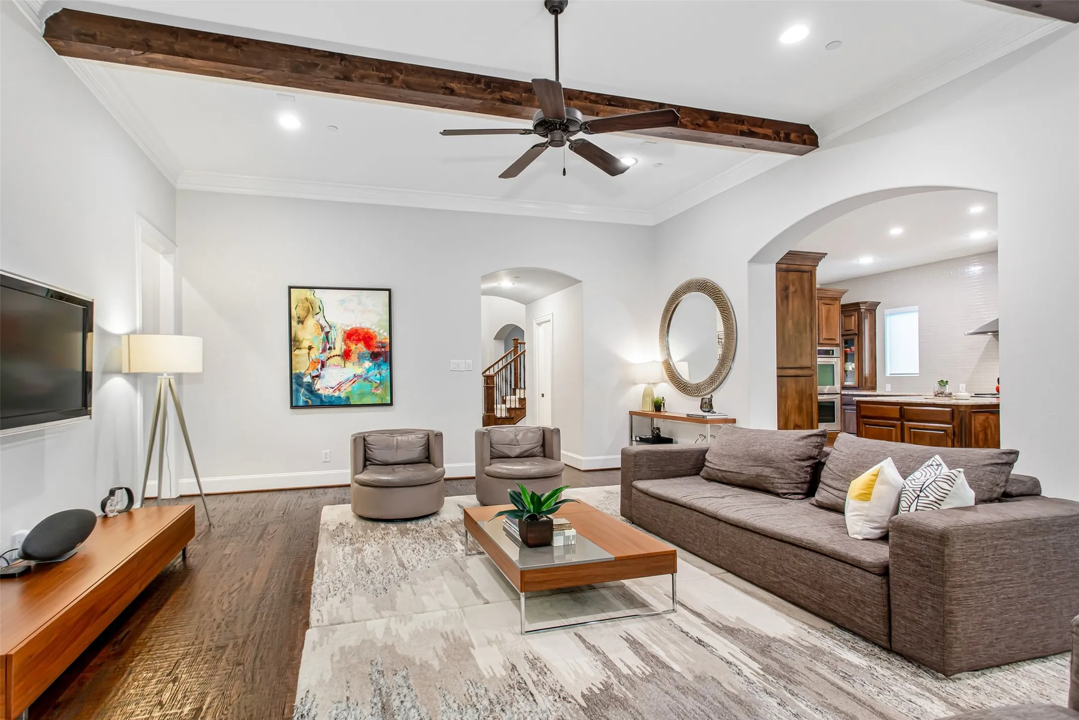 Spacious living area featuring wood-finish flooring, exposed ceiling beams, and crown molding