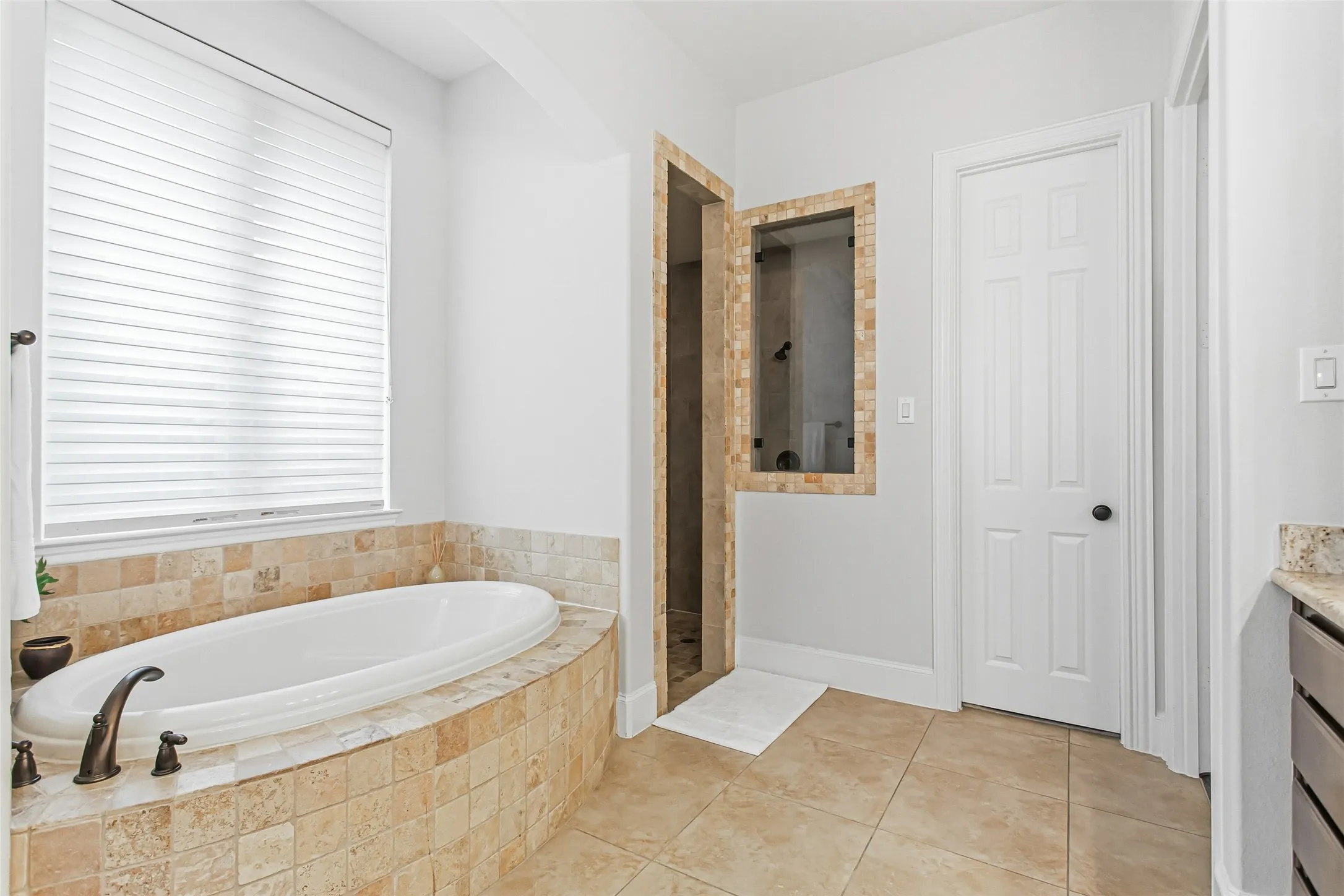 Bathroom featuring an oval drop-in soaking tub with bronze fixtures, surrounded by a tiled deck