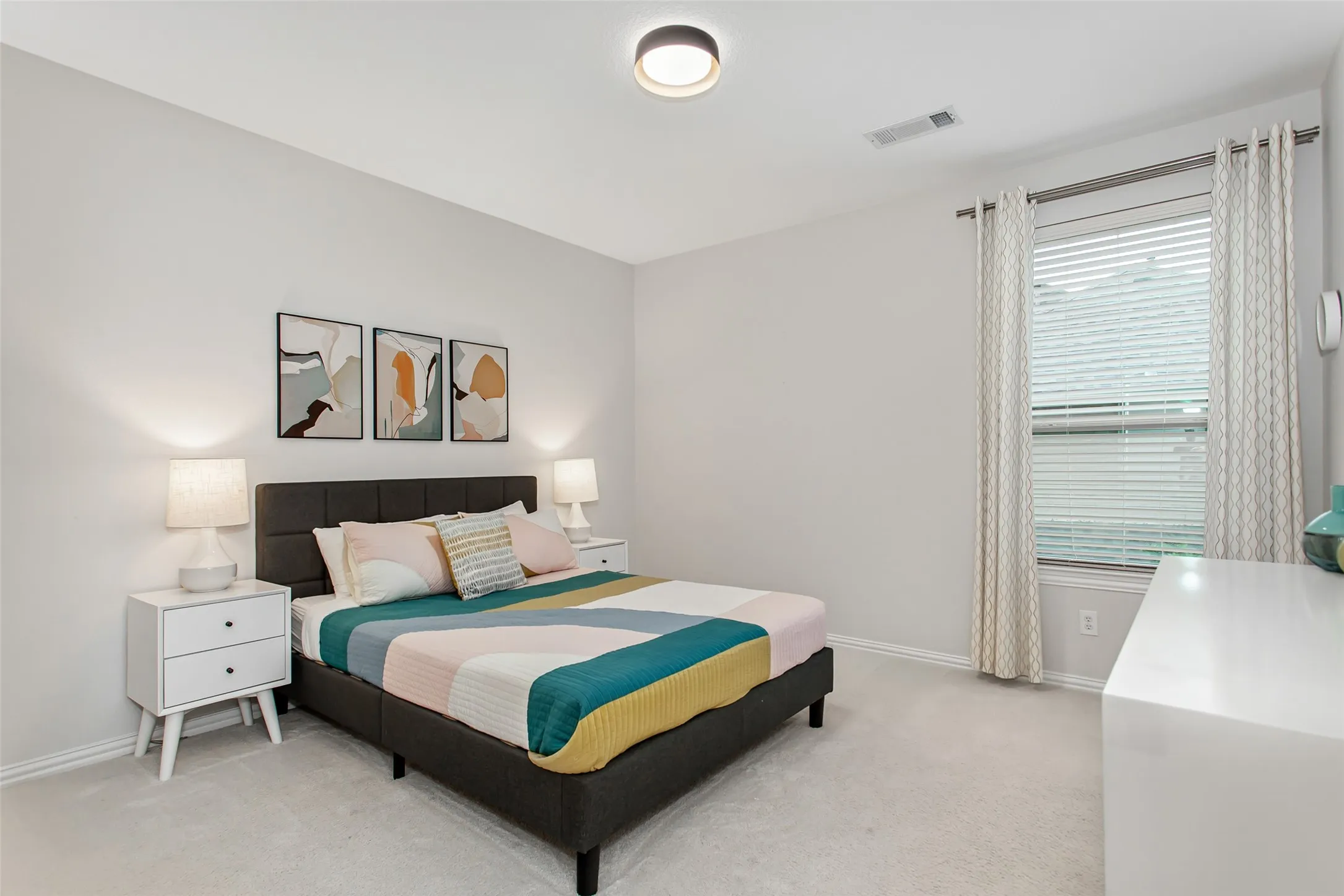 Bright room featuring neutral wall paint, light-colored carpeting, a single window with blinds and drapes, and a contemporary flush-mount ceiling light fixture