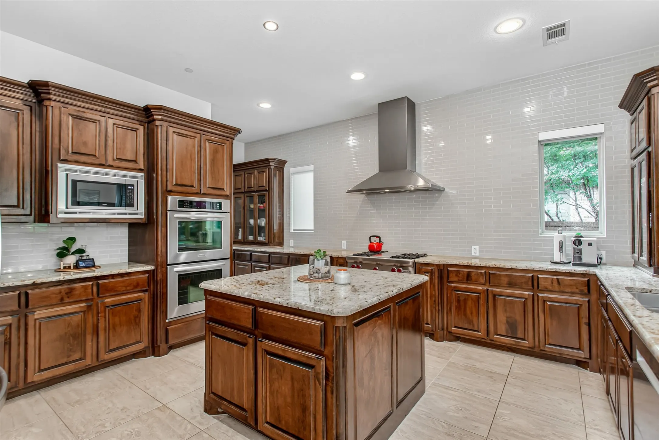 Gourmet kitchen featuring rich wood cabinetry, stainless steel appliances, a central island with a stone countertop, tile flooring, and a subway tile backsplash