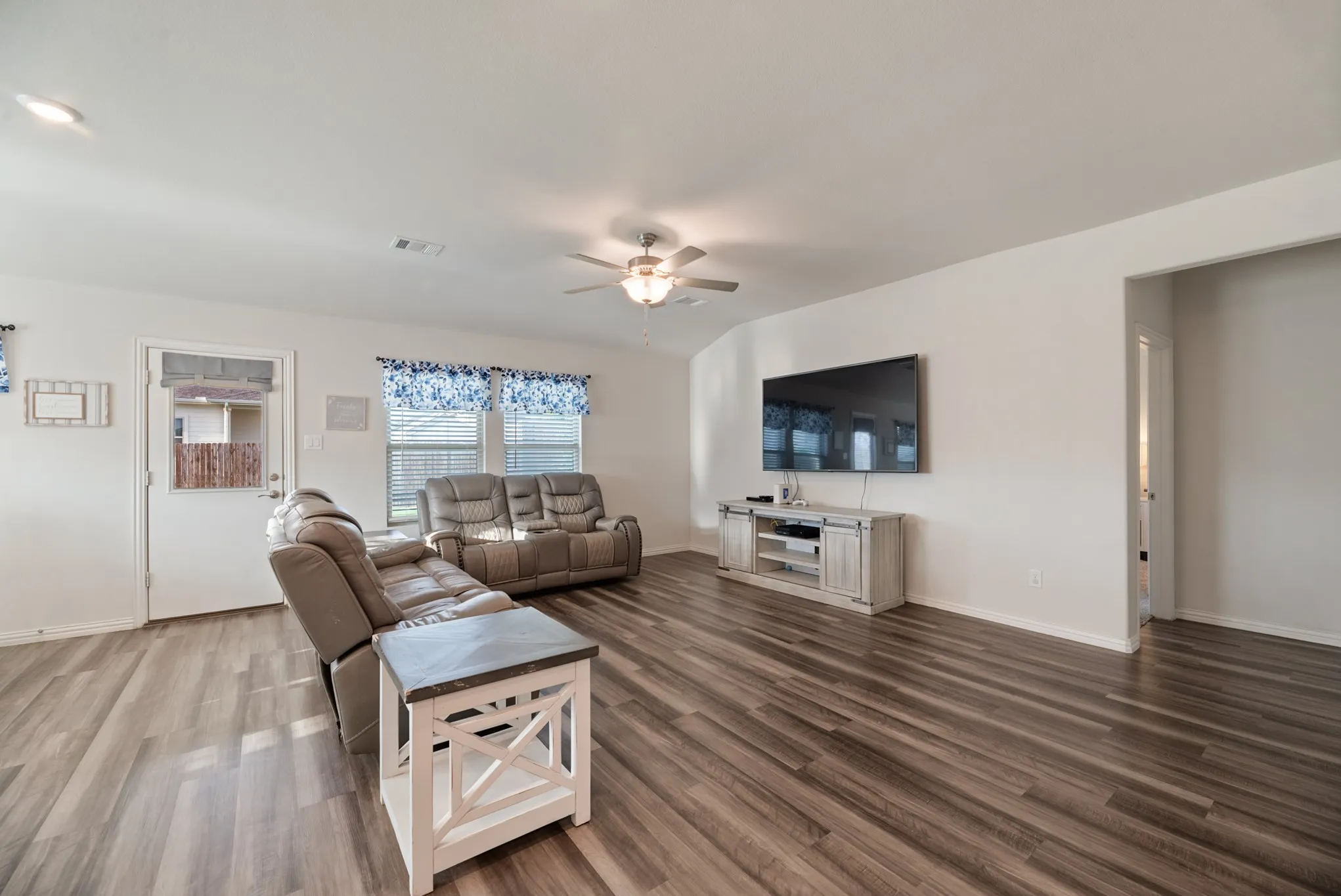 Spacious interior featuring wood-finish flooring, white walls, and a ceiling fan with integrated lighting