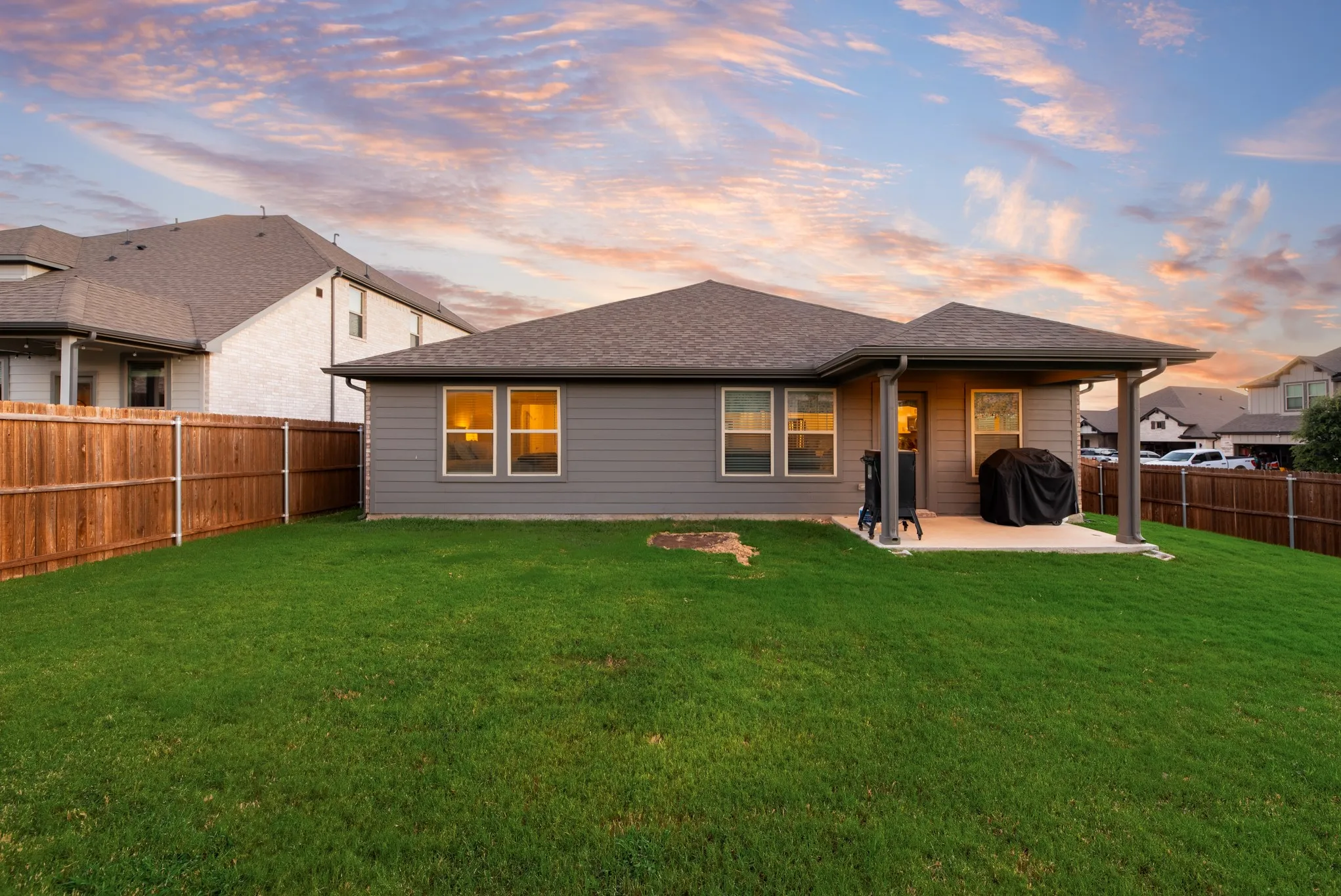 Expansive backyard with a manicured lawn, full wood fencing, and a covered patio