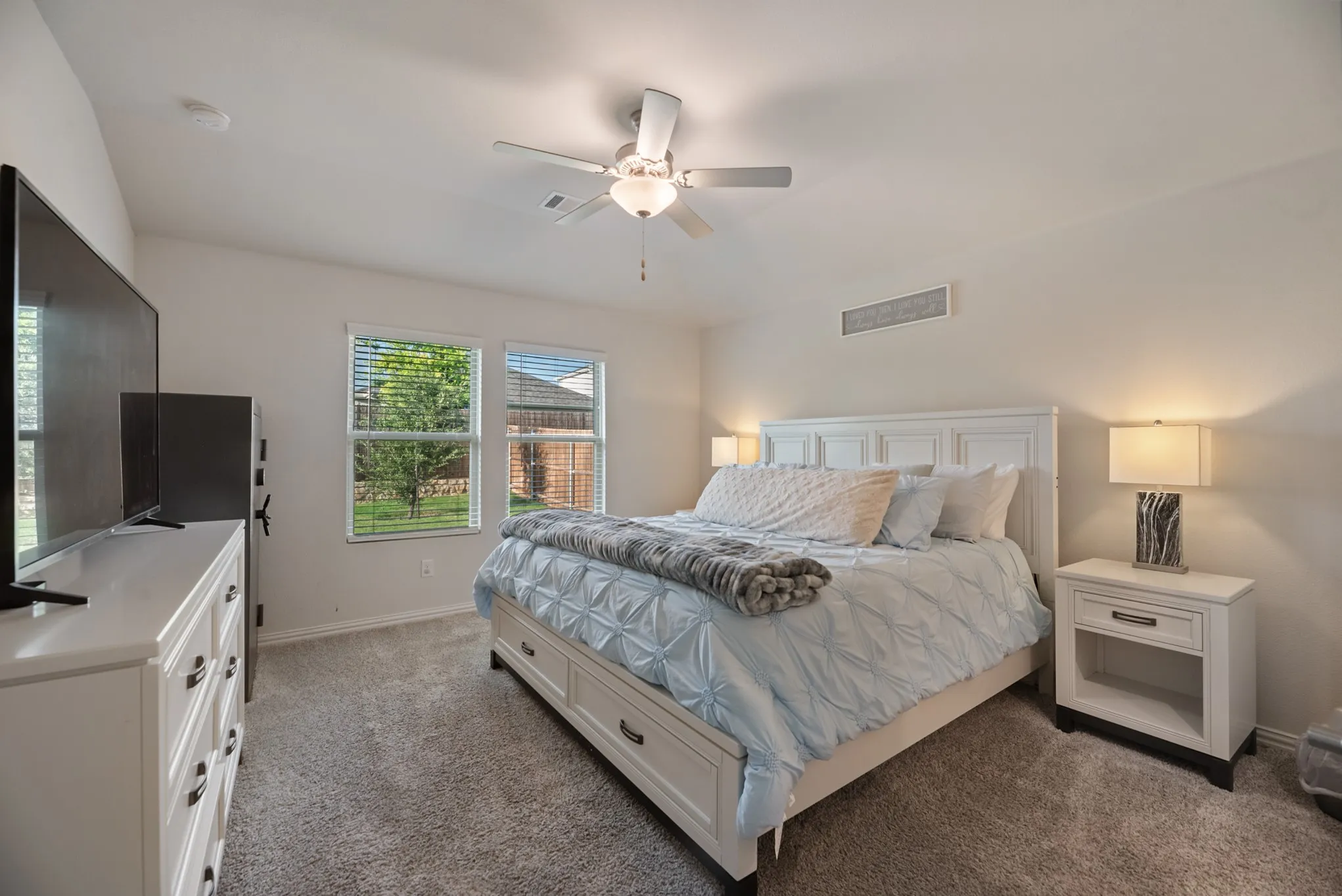 Carpeted bedroom featuring a ceiling fan with light fixture, two windows with blinds, and white painted walls