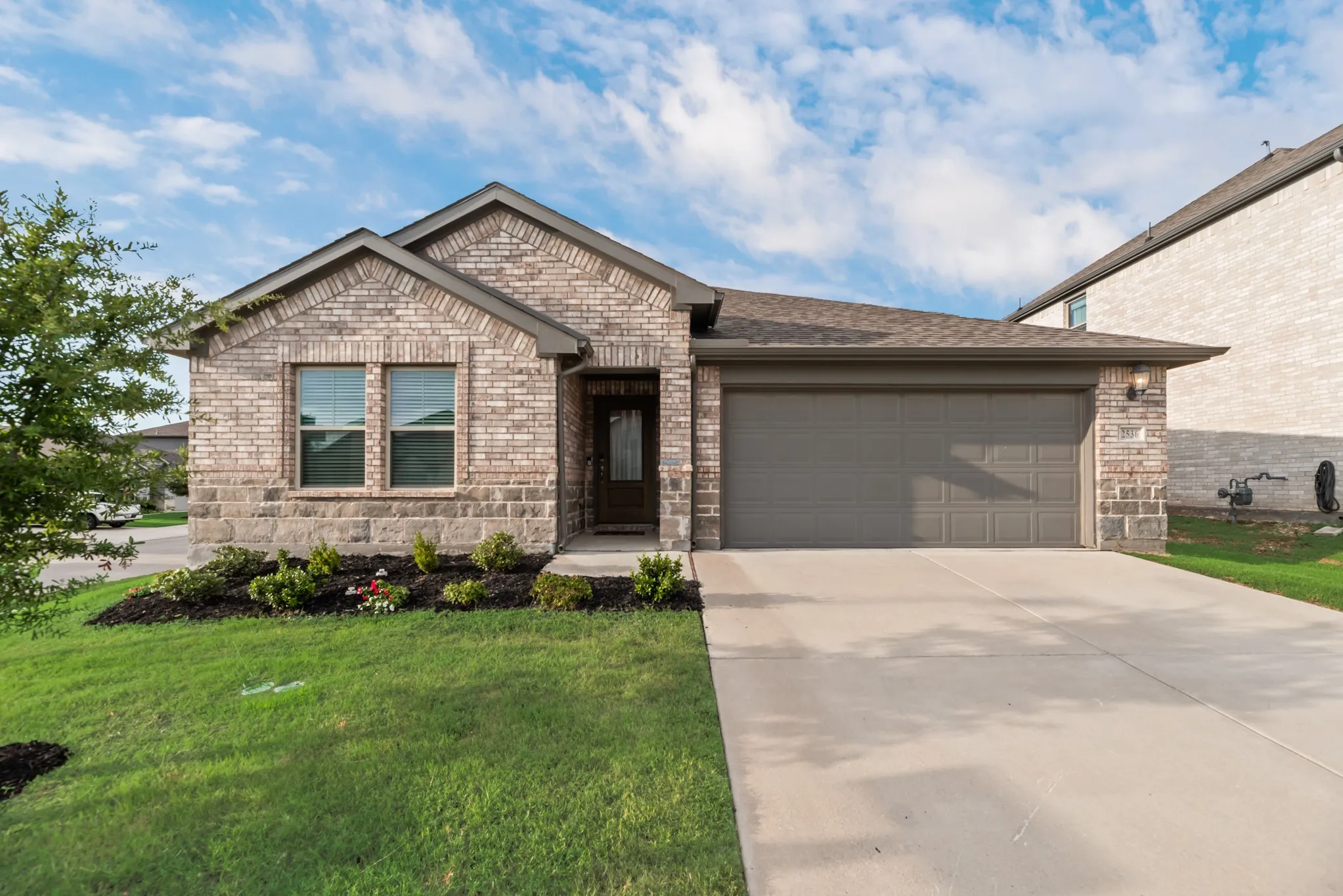 Brick and stone veneer exterior featuring a two-car garage, concrete driveway, and front lawn with landscaped beds