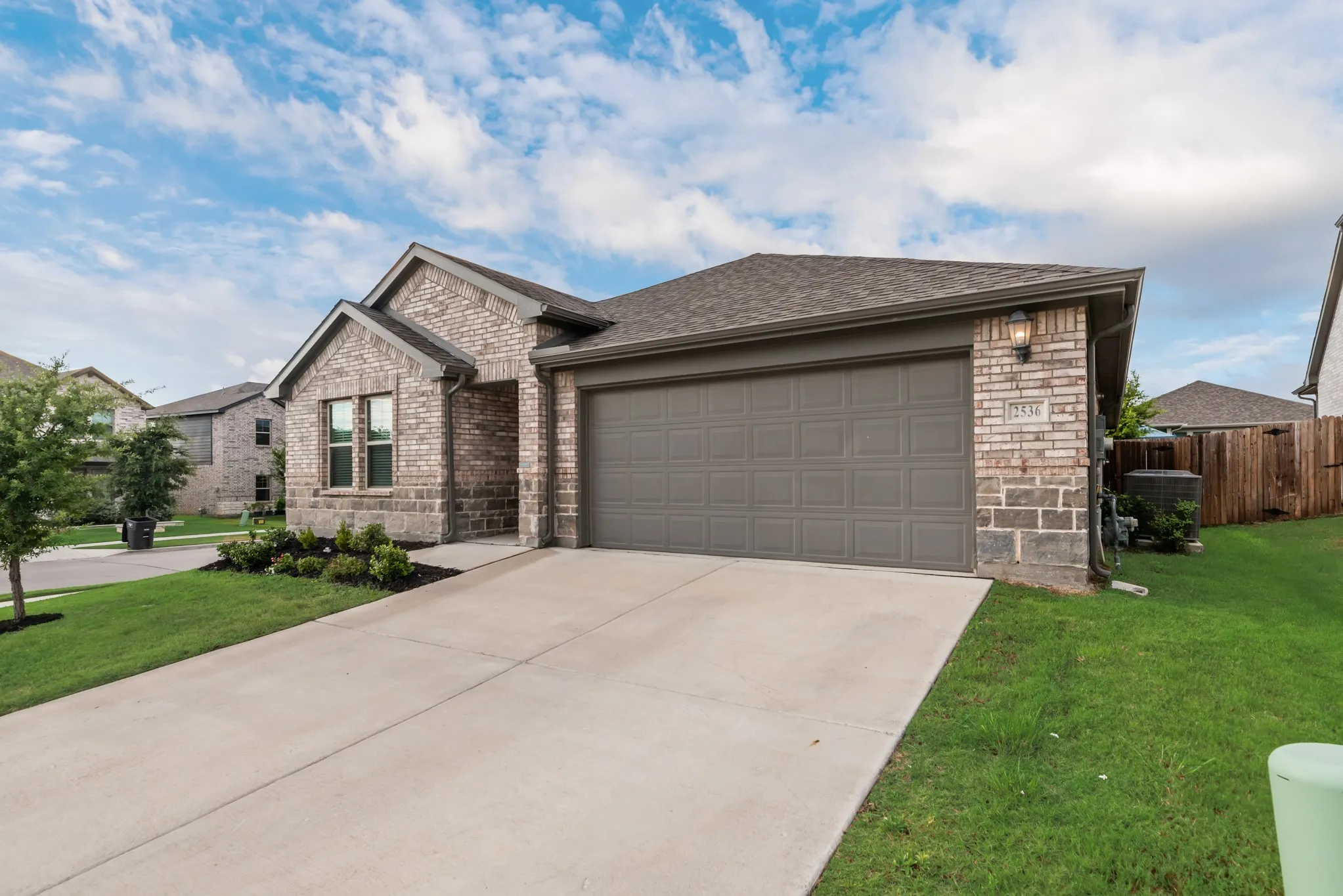 Front exterior featuring a brick facade with stone accents, a concrete driveway, an attached garage, and a gabled roofline