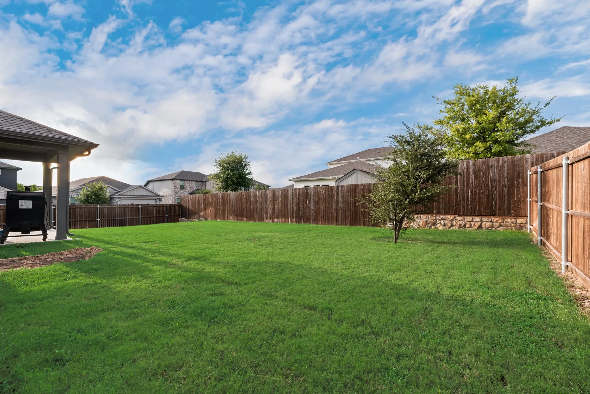 Expansive fenced backyard featuring a meticulously maintained lawn, a covered patio area with a dark-pitched roof, and a privacy fence constructed from vertical wood planks