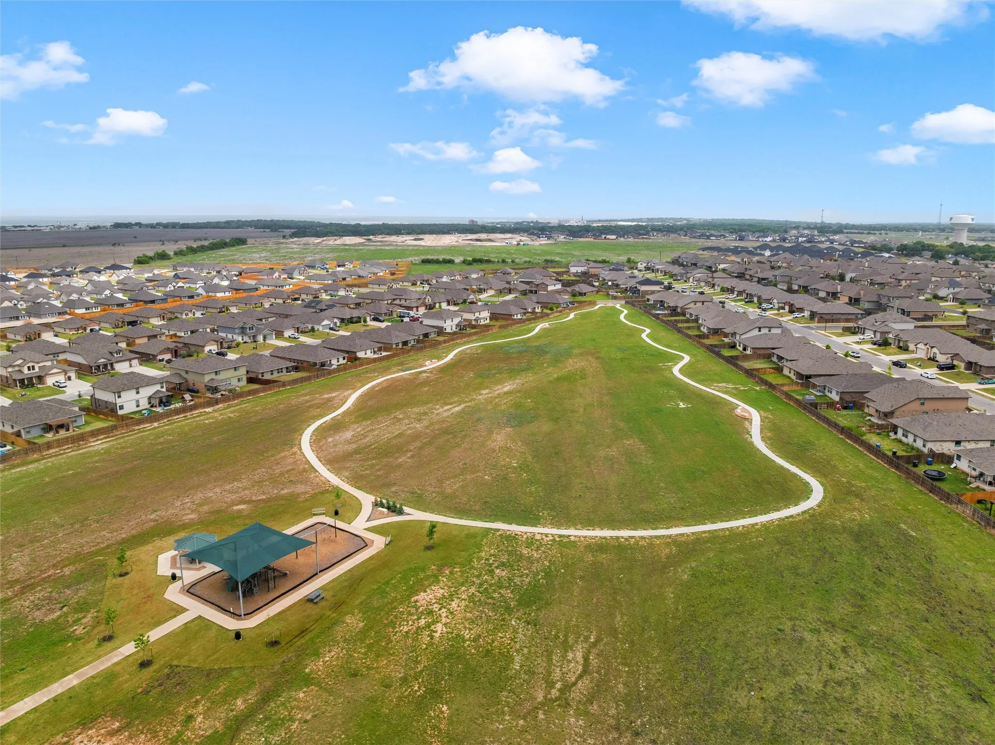 Expansive green space featuring a paved walking path, a covered pavilion, and surrounding residential properties