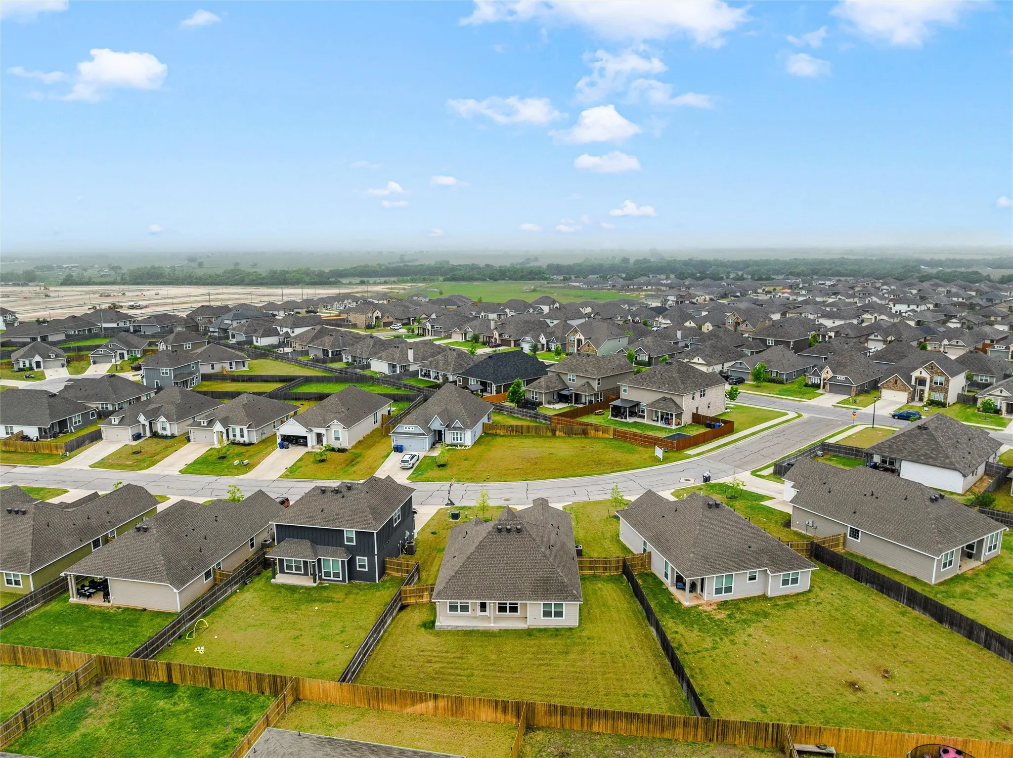 Aerial view of a residential community featuring single-story homes with dark shingle roofs, individual fenced yards, and concrete driveways