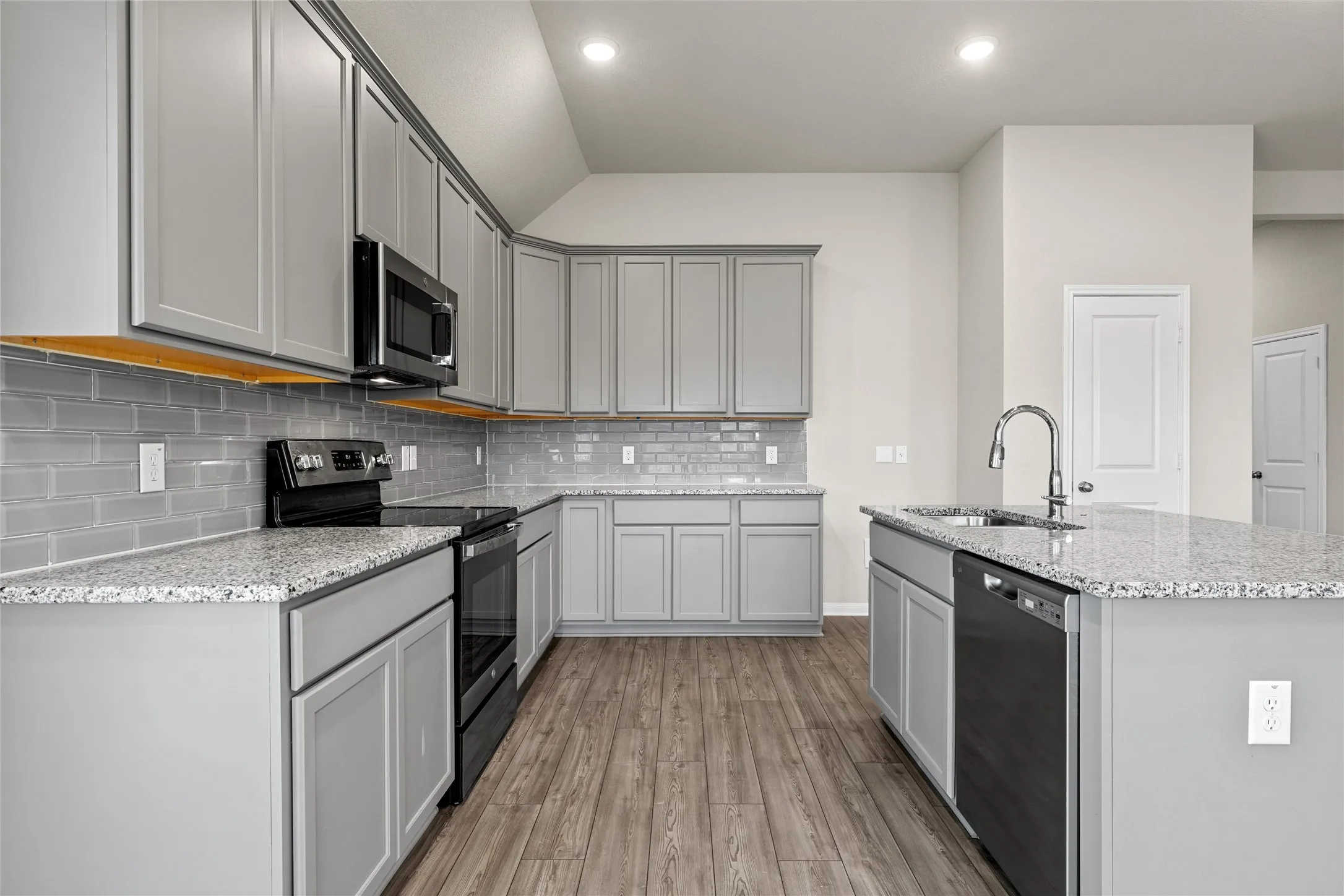 Modern kitchen featuring granite countertops, light gray cabinetry, stainless steel appliances, a subway tile backsplash, and wood-finish flooring