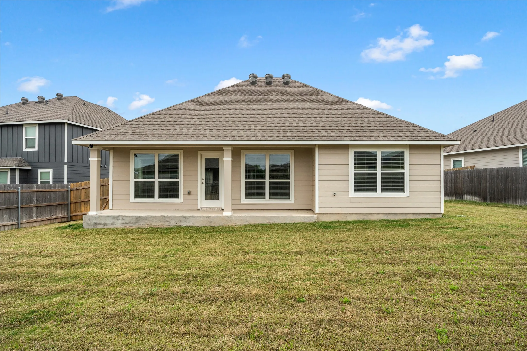 Rear exterior featuring a covered concrete patio, light-colored horizontal siding, and multiple windows with white trim