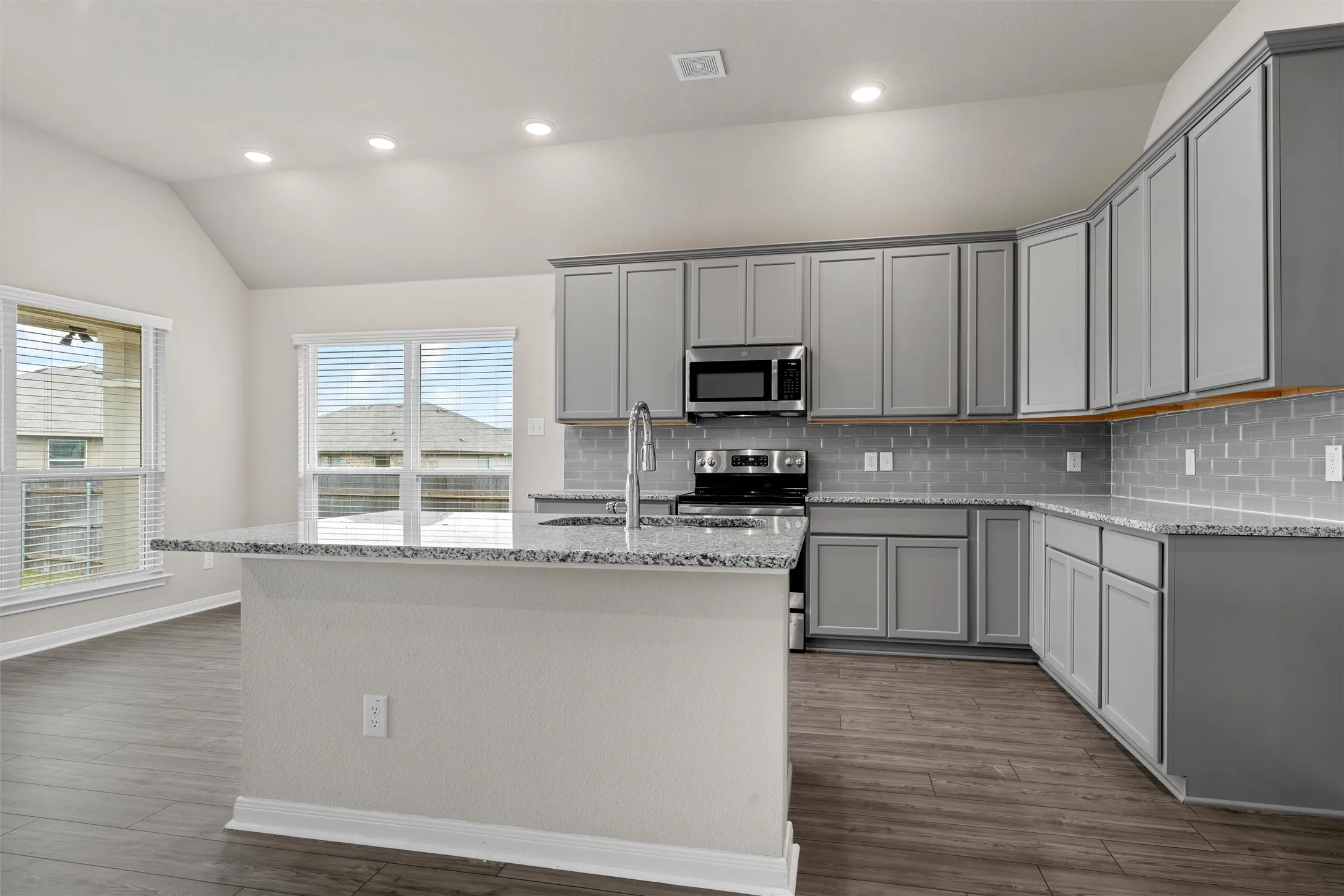 Kitchen featuring an island with a breakfast bar, granite countertops, gray shaker-style cabinetry, stainless steel appliances, and wood-finish flooring