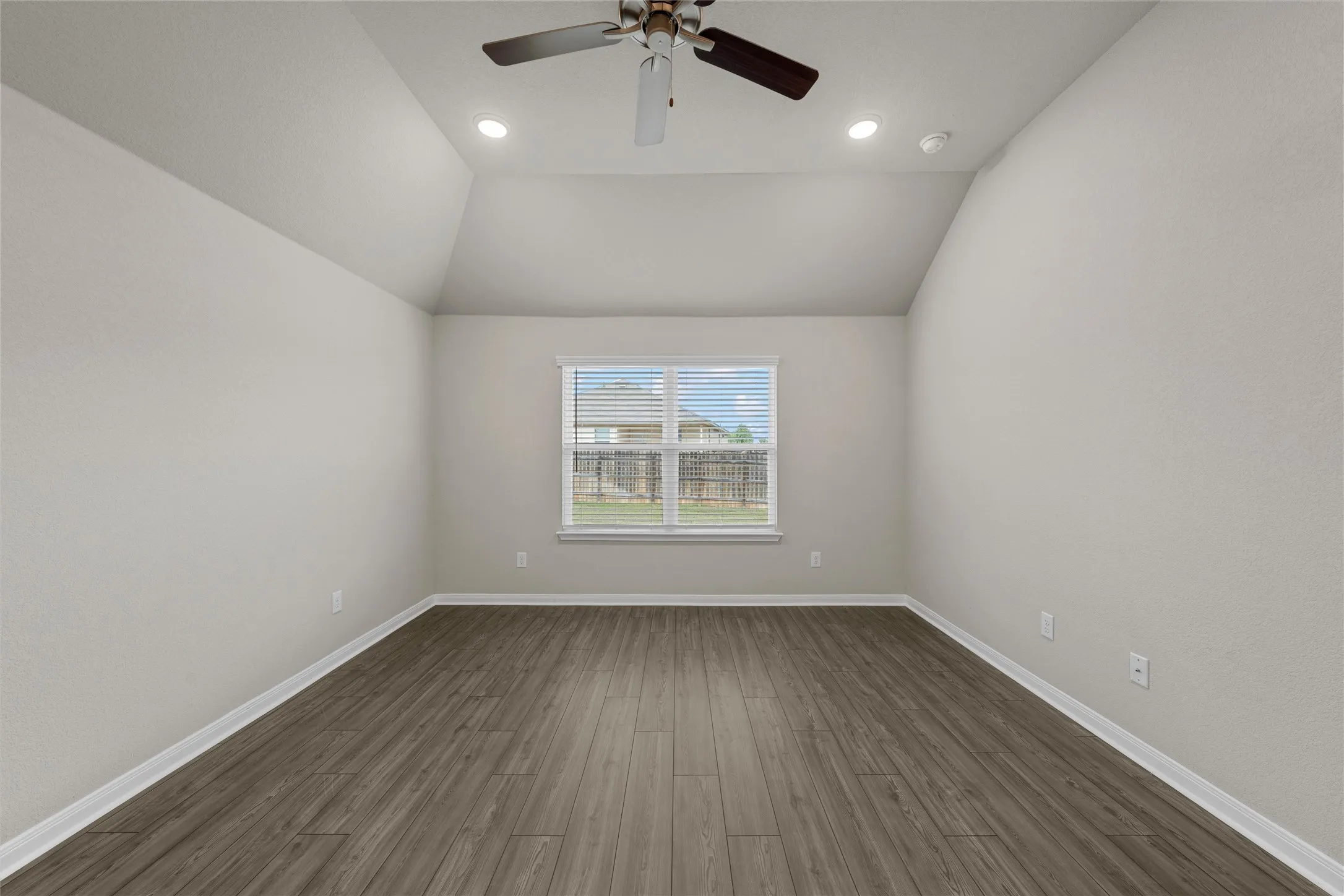 Spacious interior room featuring a vaulted ceiling with recessed lighting and a ceiling fan, wood-finish flooring, a window with blinds, and light-toned wall finishes