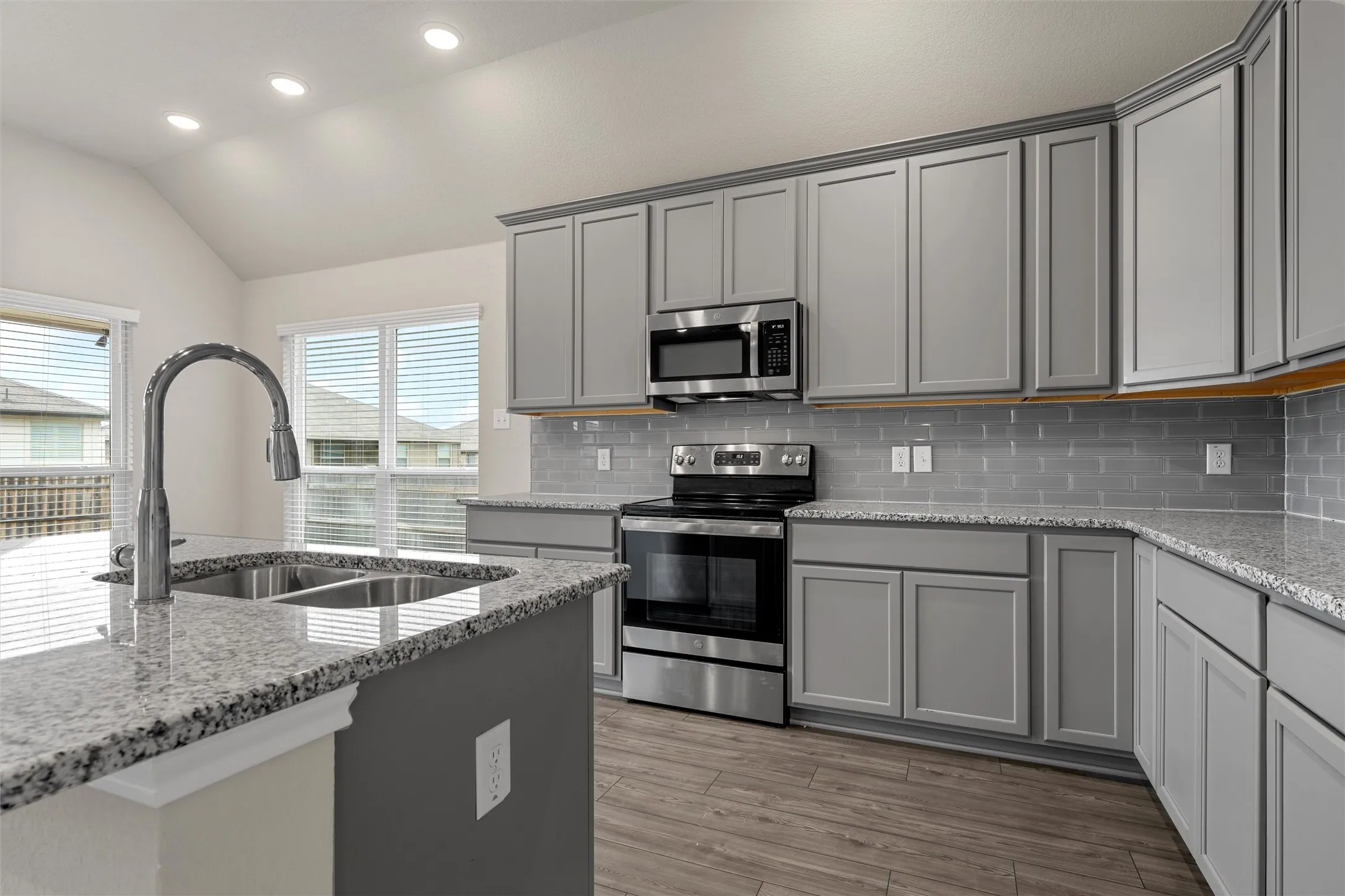 Kitchen featuring light gray cabinetry, stainless steel appliances, granite countertops, and a gray subway tile backsplash