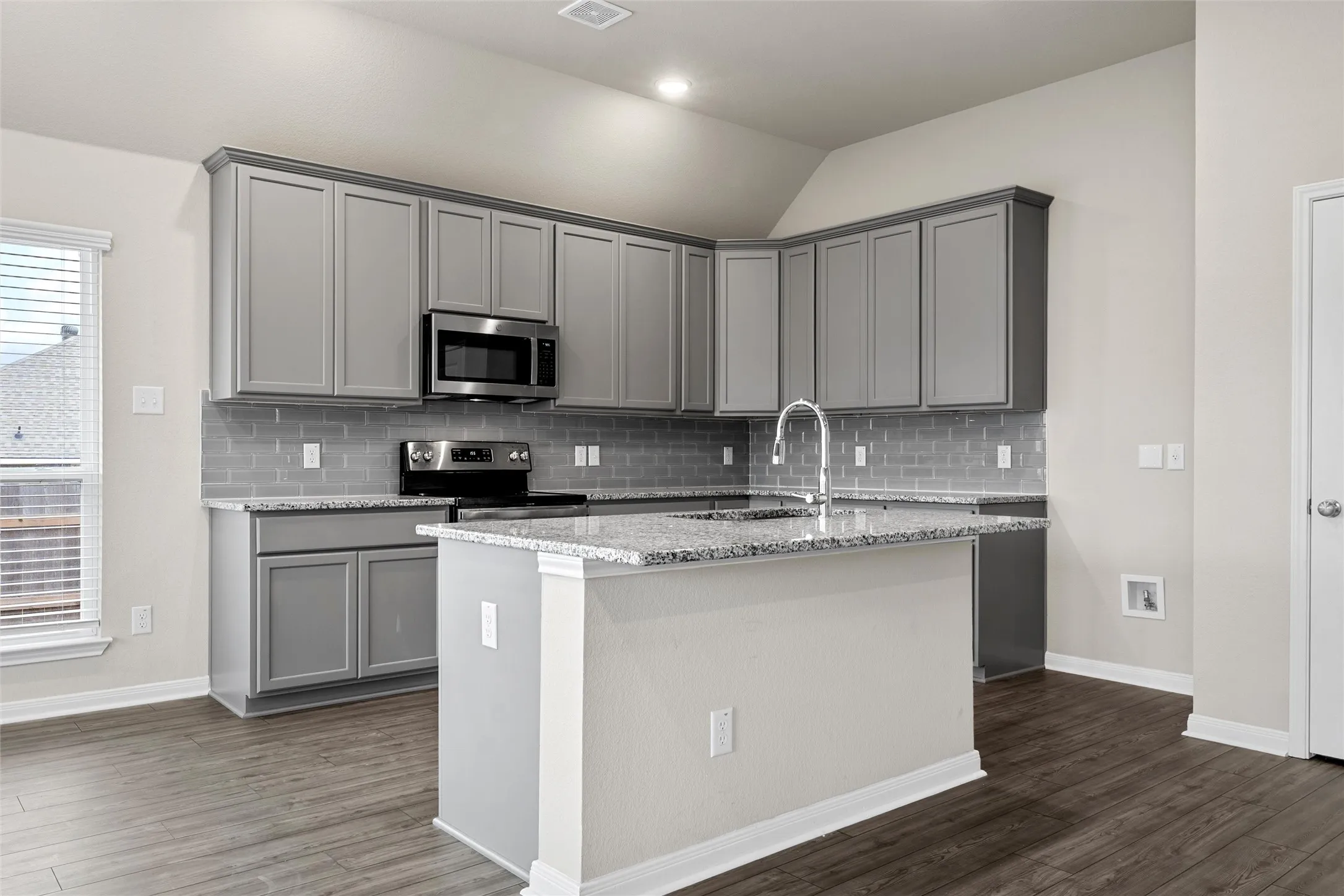 Kitchen featuring a central island, light gray cabinetry, stainless steel appliances, a subway tile backsplash, and wood-finish flooring