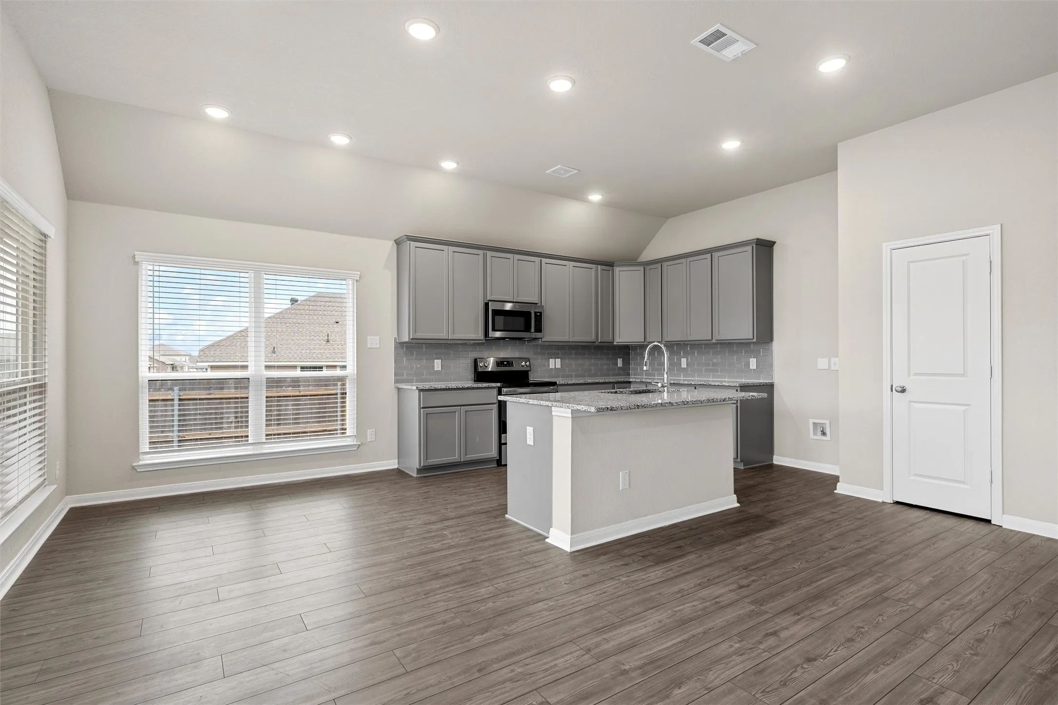 Open-concept kitchen and living area featuring grey cabinetry, stainless steel appliances, a center island with a sink, wood-finish flooring, and recessed lighting
