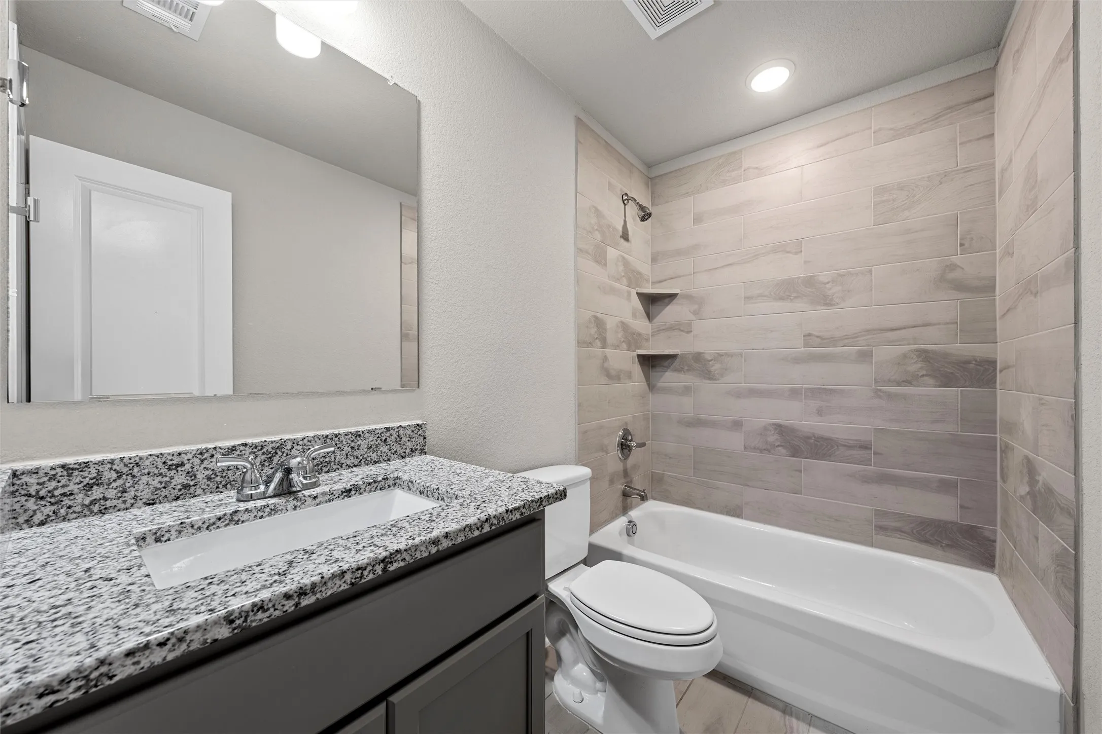 Bathroom featuring a single vanity with a granite-style countertop, undermount sink, and chrome-finish faucet