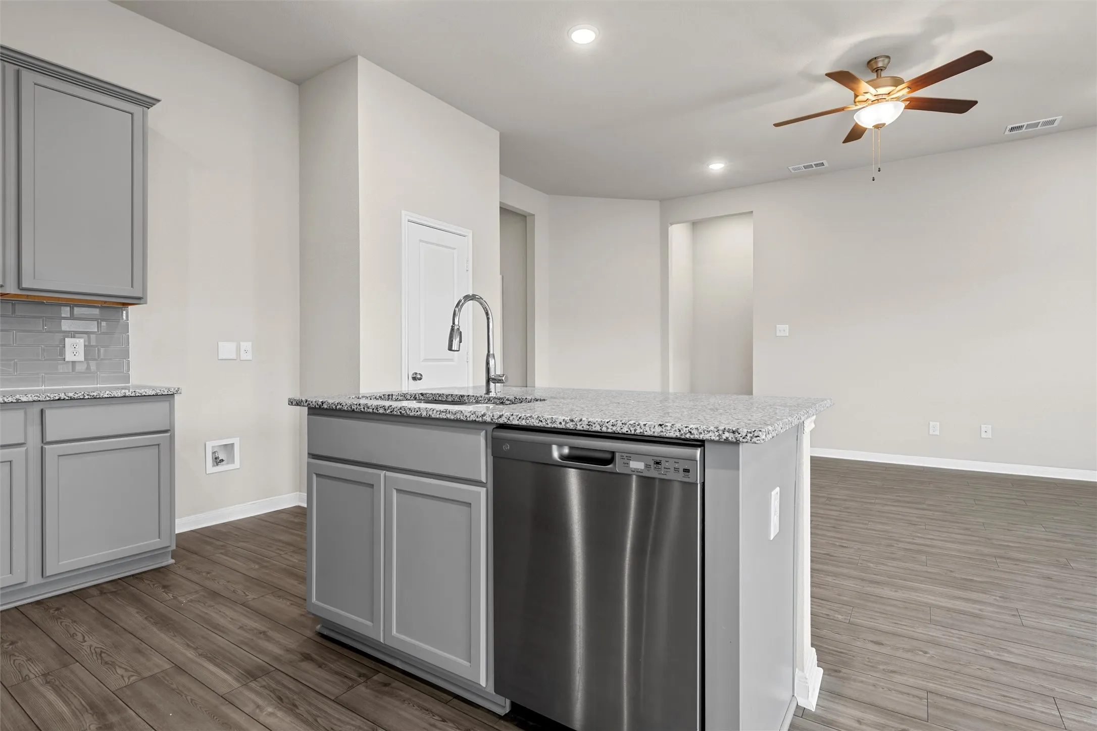 Kitchen island featuring a stainless steel dishwasher, an integrated sink with a gooseneck faucet, and a speckled countertop