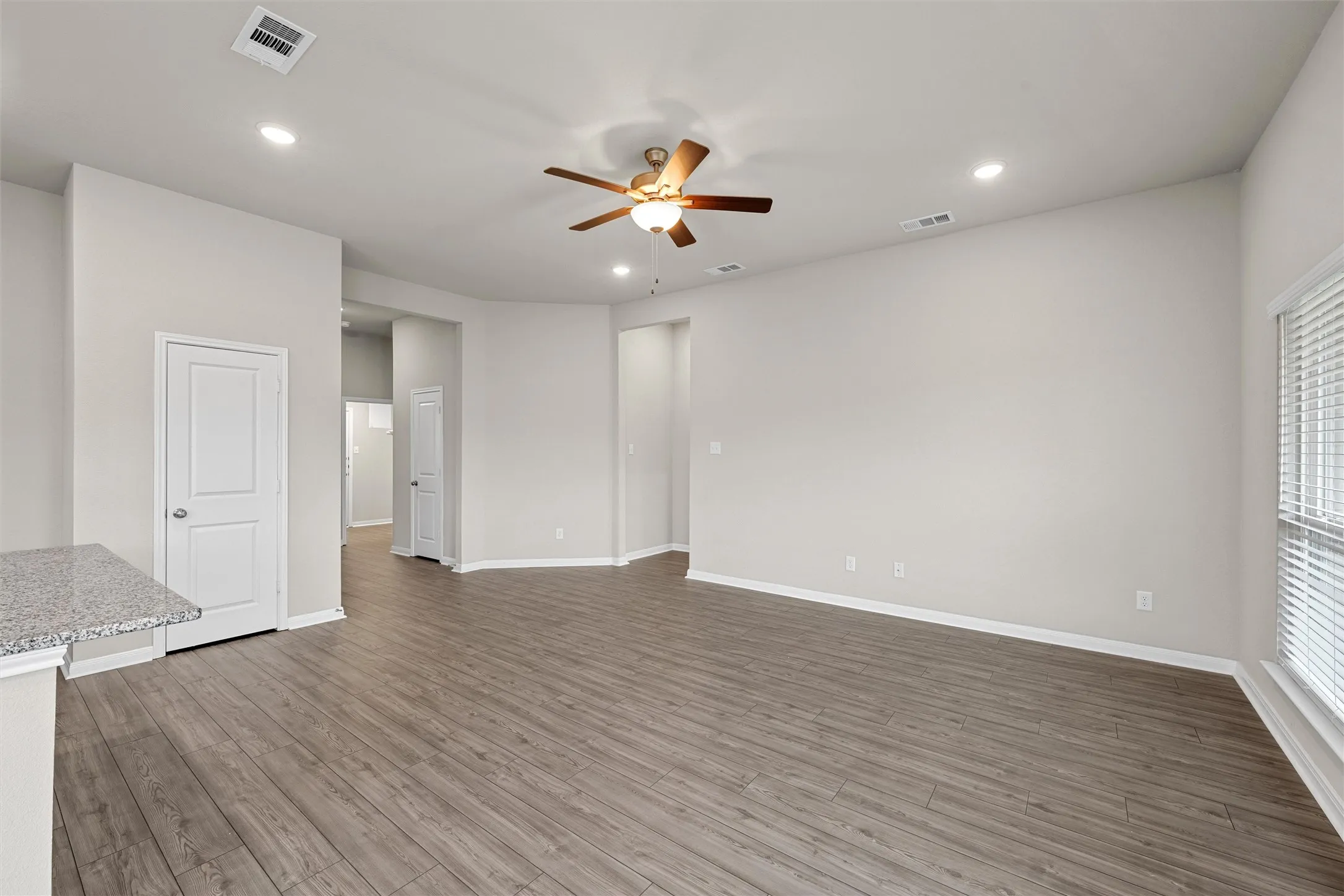 Spacious interior featuring wood-finish flooring, a ceiling fan with light, recessed lighting, and a window with blinds
