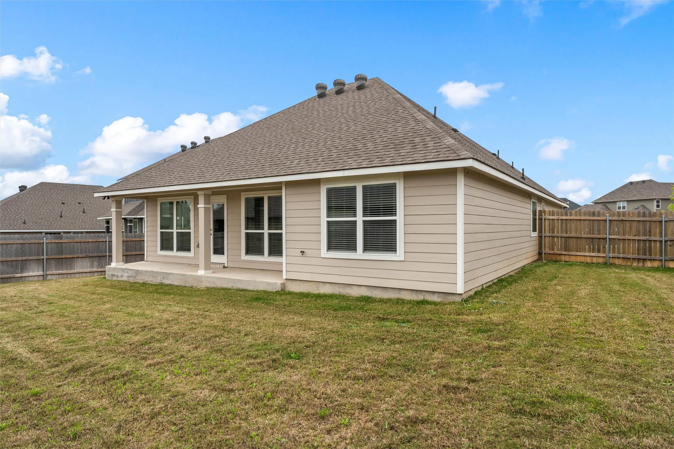 Expansive rear yard featuring a covered patio, multiple windows, and a wood privacy fence
