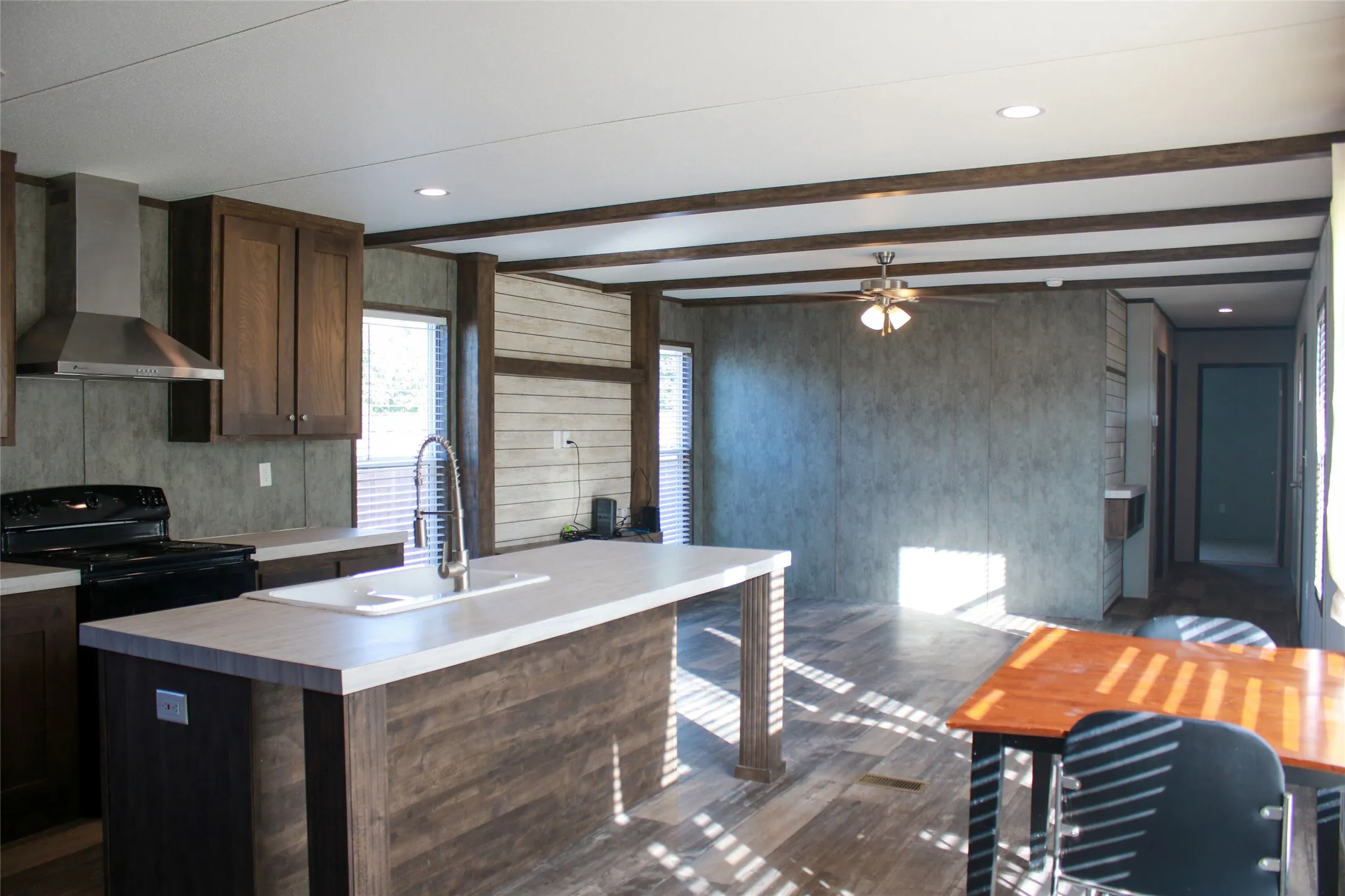 Kitchen with wood-finish cabinetry, stainless steel range hood, and a kitchen island featuring an integrated sink
