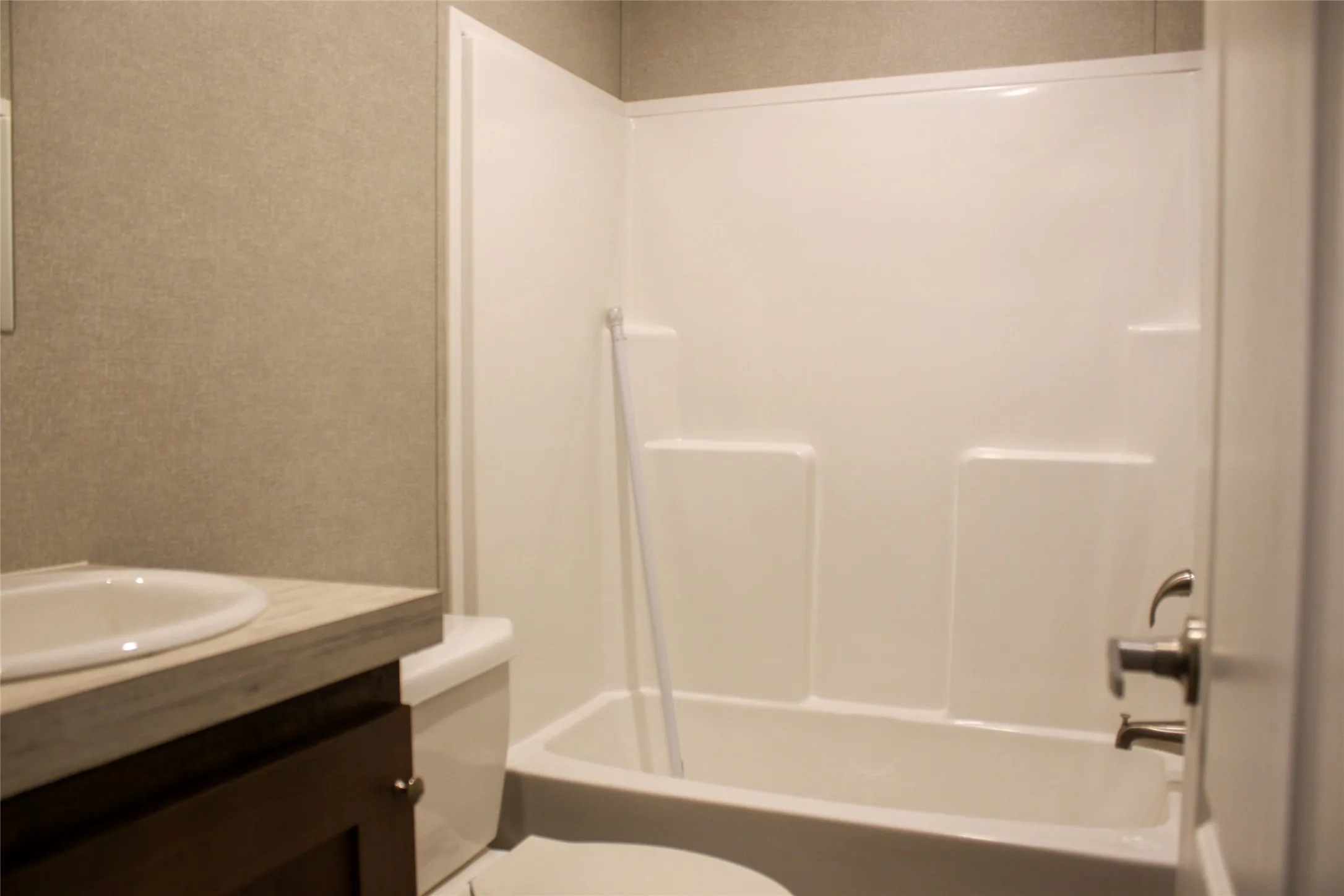 Bathtub with integrated shower surround, vanity with an integrated sink, and dark wood-finish cabinetry