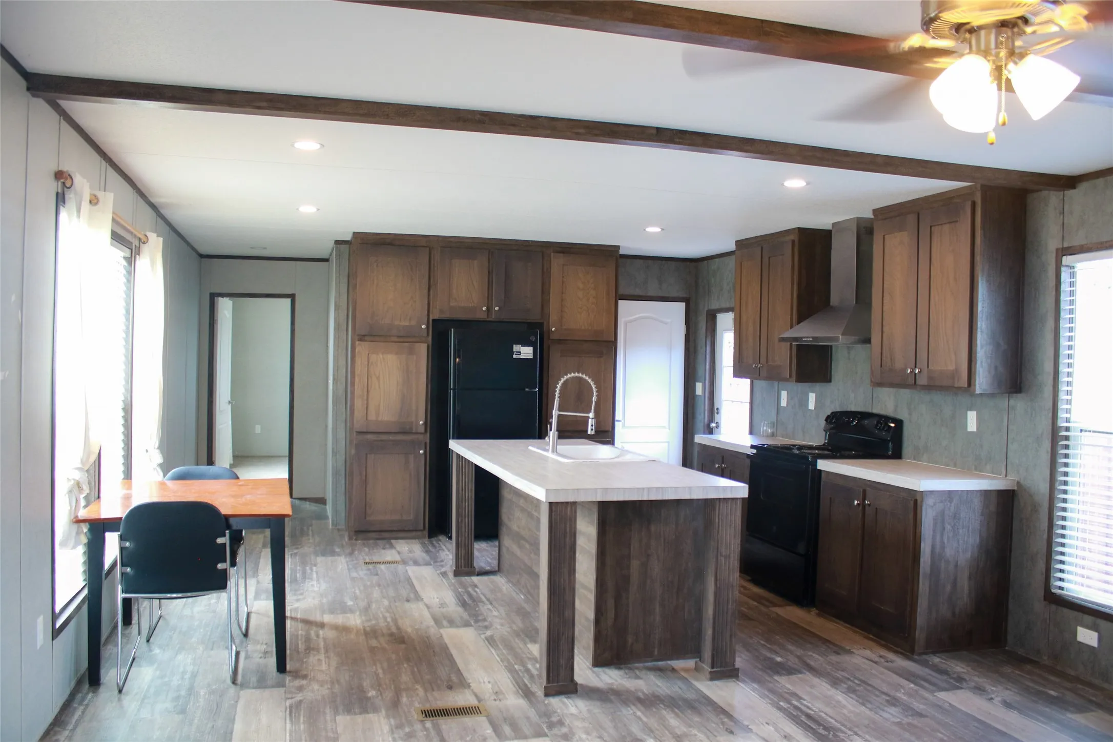 Wood-finish flooring, dark wood cabinetry, white countertops, kitchen island with sink, and recessed lighting
