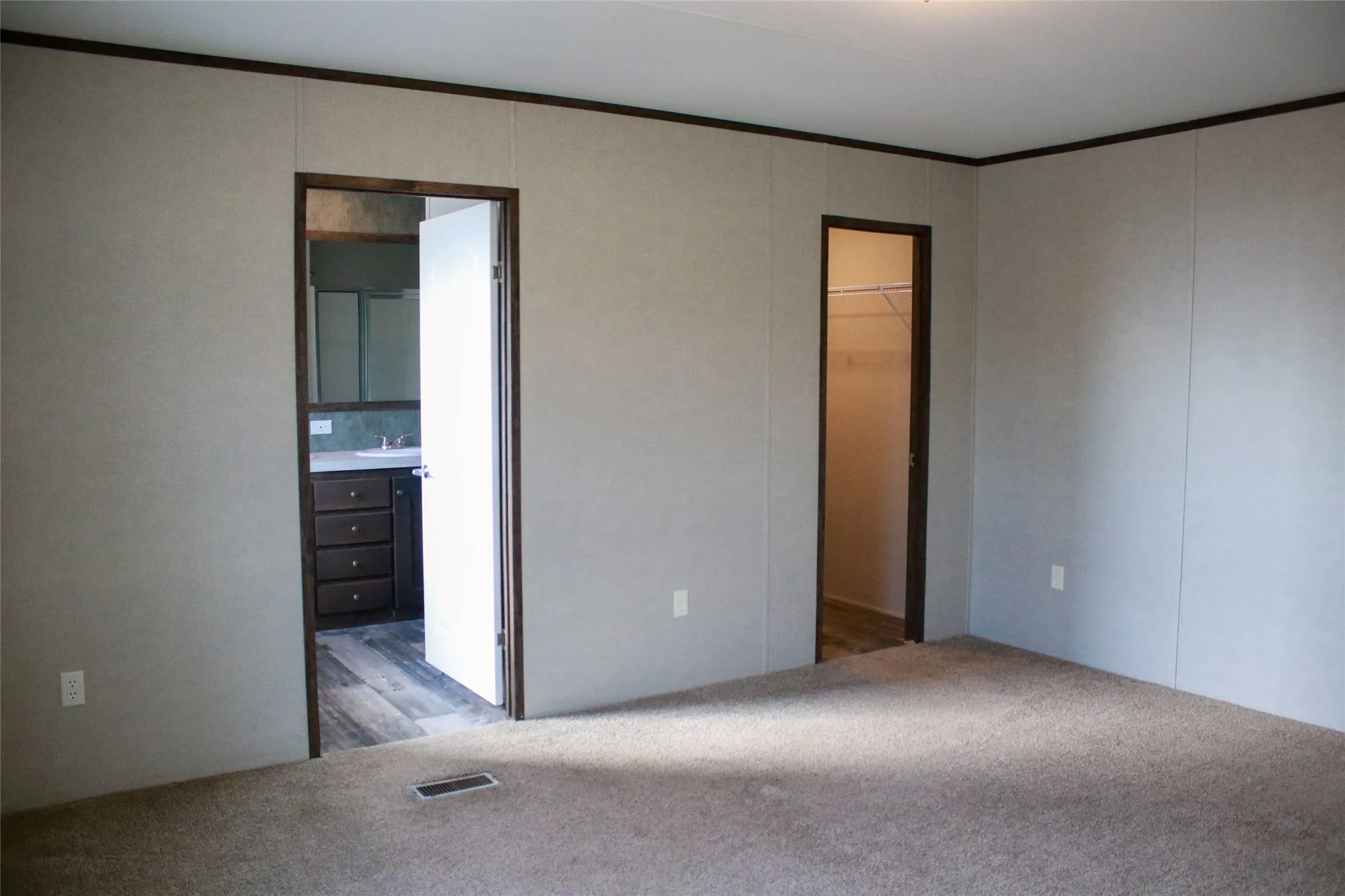 Carpeted room with panel walls and dark trim, featuring a doorway to a bathroom with a dark wood-finish vanity and a doorway to a closet with built-in shelving