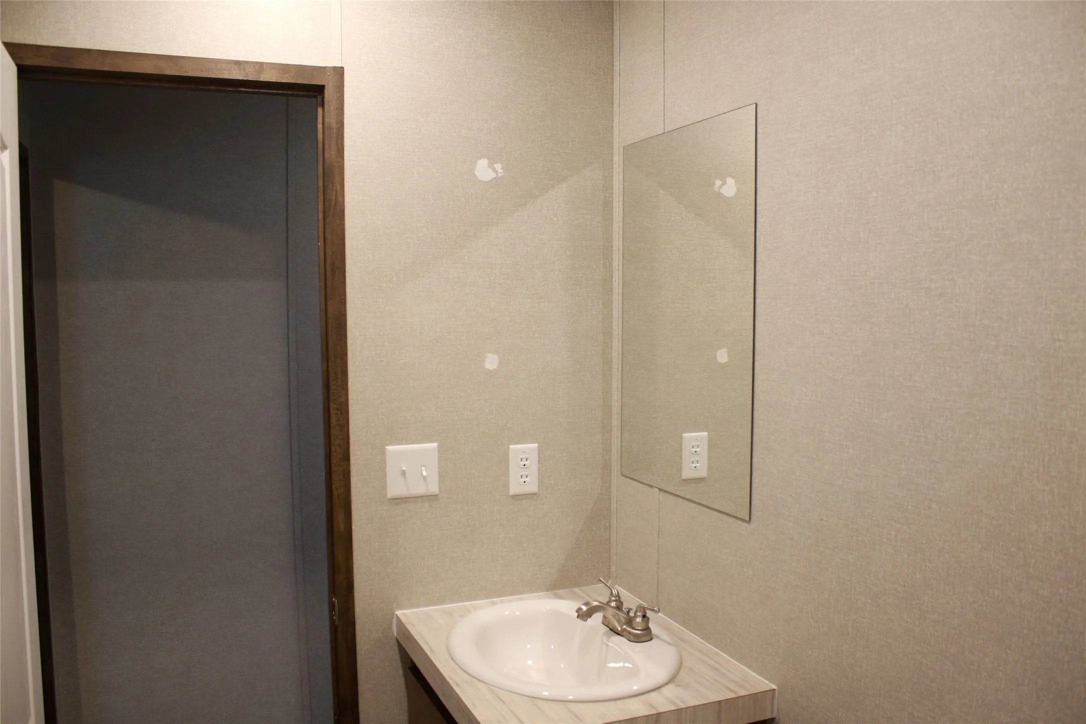 Single-basin vanity with a light wood-finish countertop, polished chrome faucet, and rectangular wall-mounted mirror