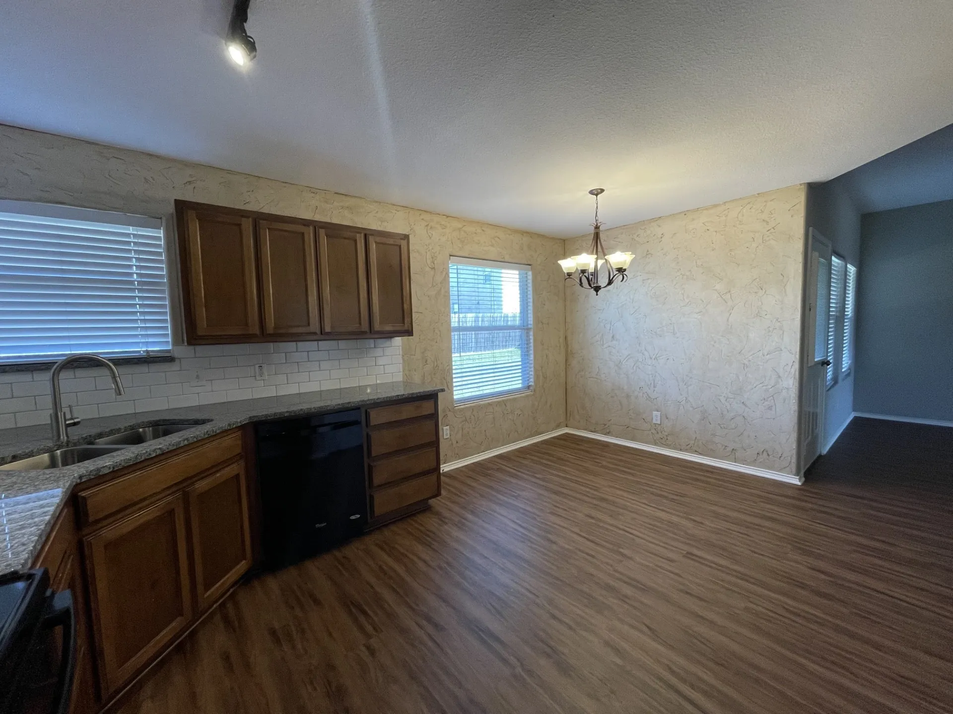 Kitchen and dining area featuring wood-finish flooring, wood cabinetry, granite countertops, subway tile backsplash, and a modern chandelier