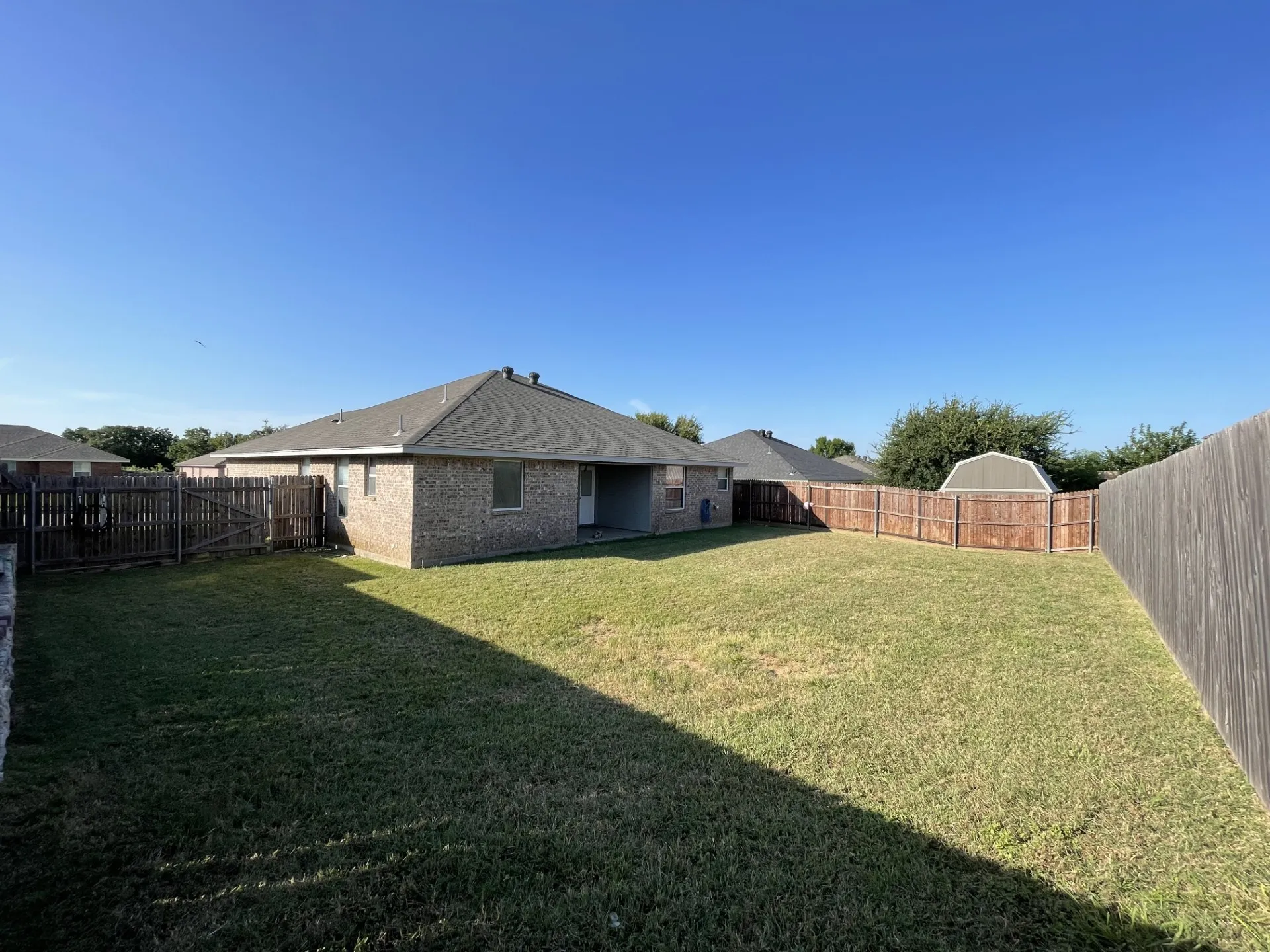 Expansive backyard featuring a manicured lawn, full privacy fencing, and a detached storage shed