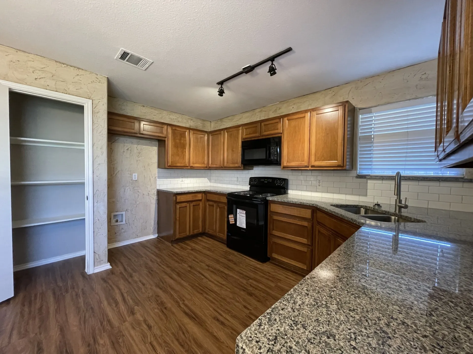Kitchen featuring wood-finish flooring, wood cabinetry, granite countertops, and a subway tile backsplash