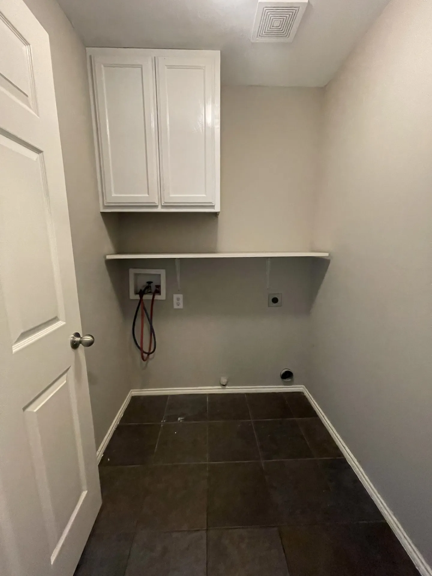 Utility space featuring dark-toned tile flooring, light neutral wall paint, and white upper cabinetry