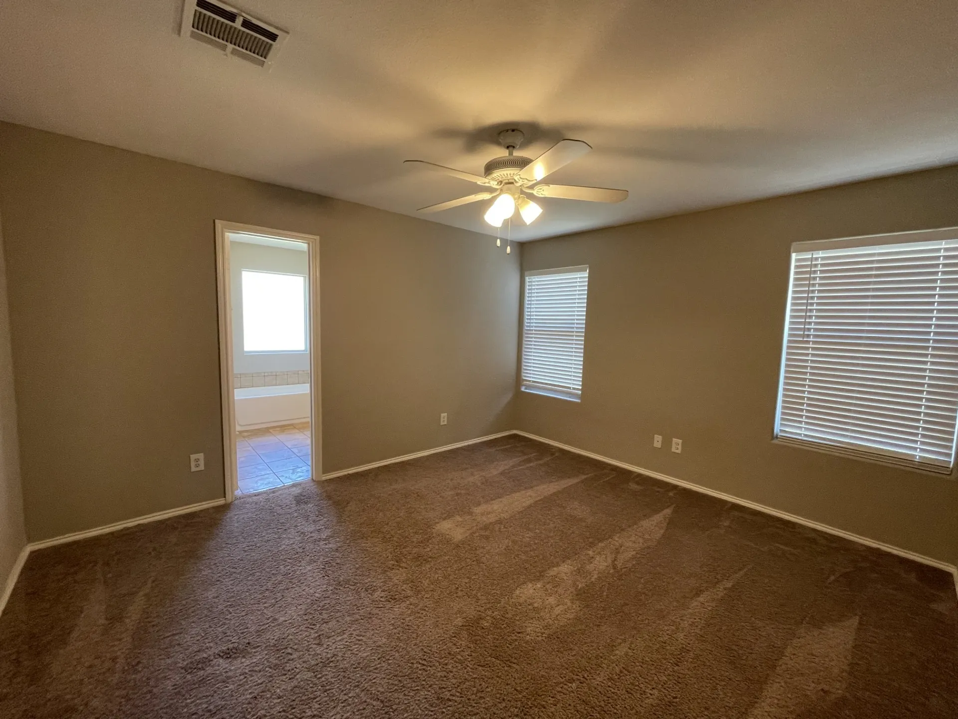 Spacious room featuring neutral wall paint, brown carpet, white baseboards, and two windows with blinds