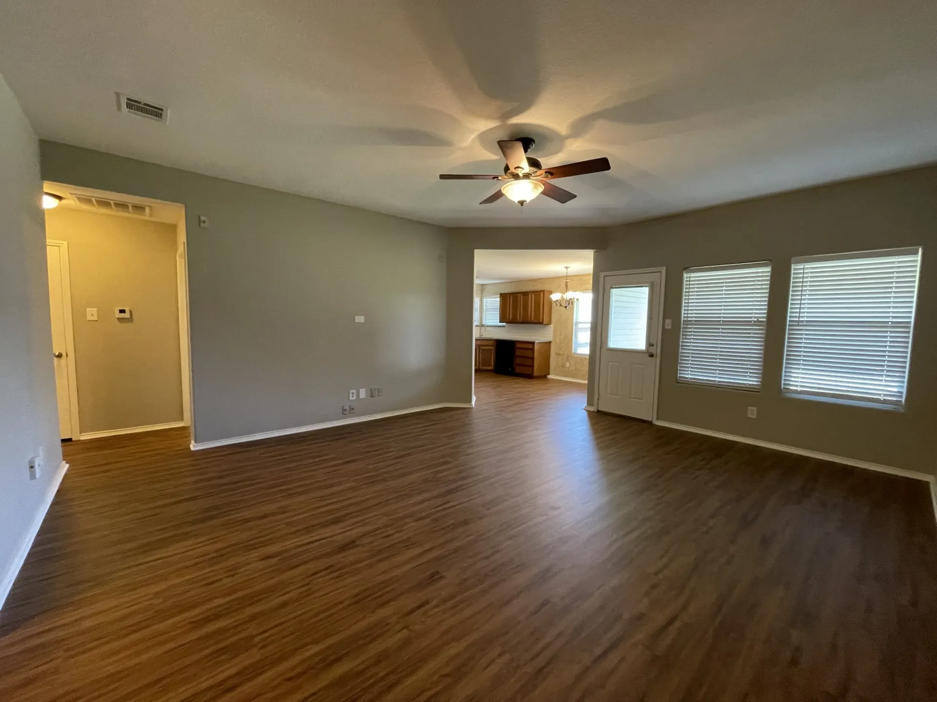 Spacious living area featuring wood-finish flooring, neutral wall tones, and a ceiling fan with integrated lighting
