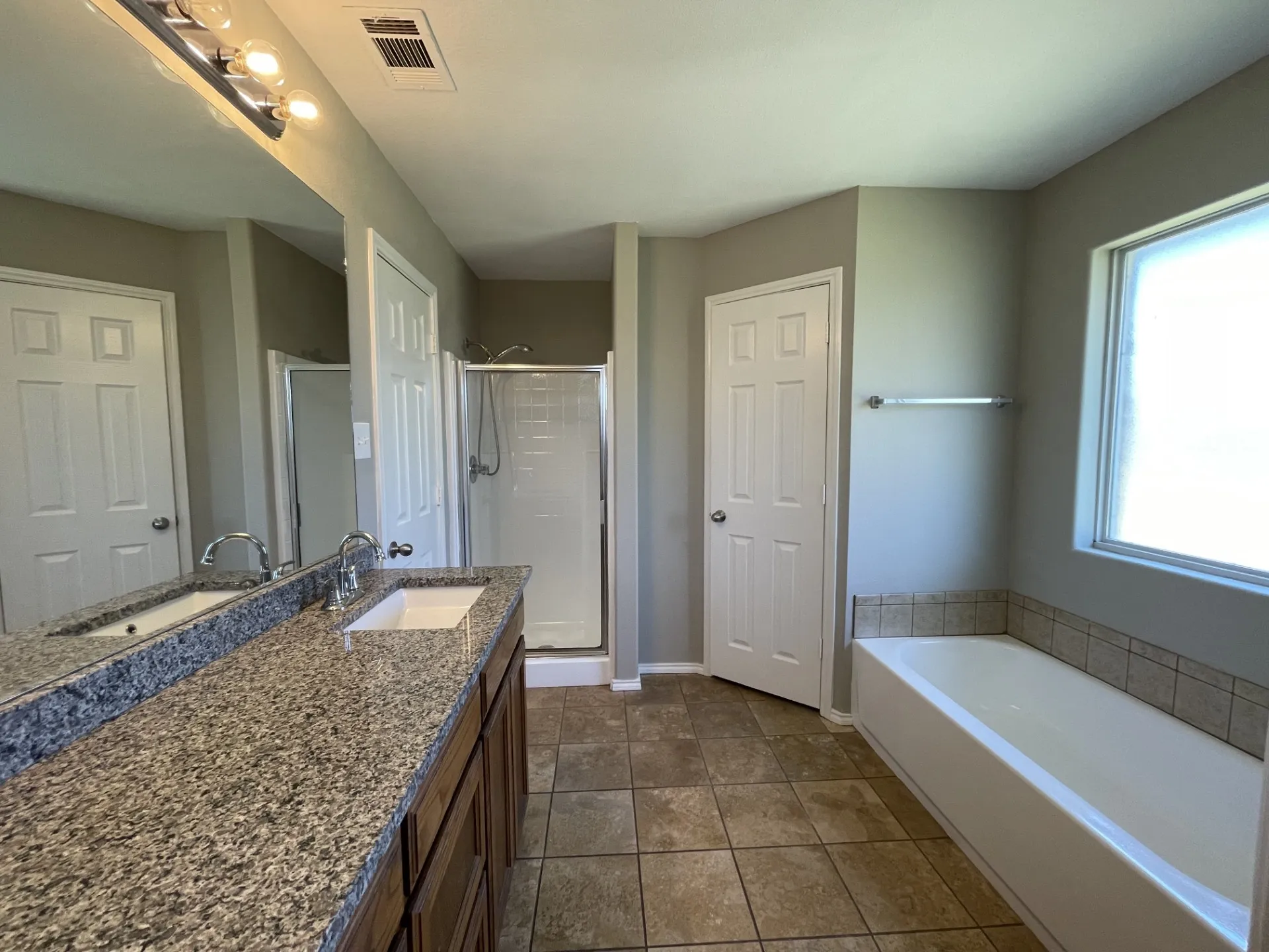 Spacious bathroom featuring a dual vanity with granite-finish countertop, undermount sinks, and a full-width mirror