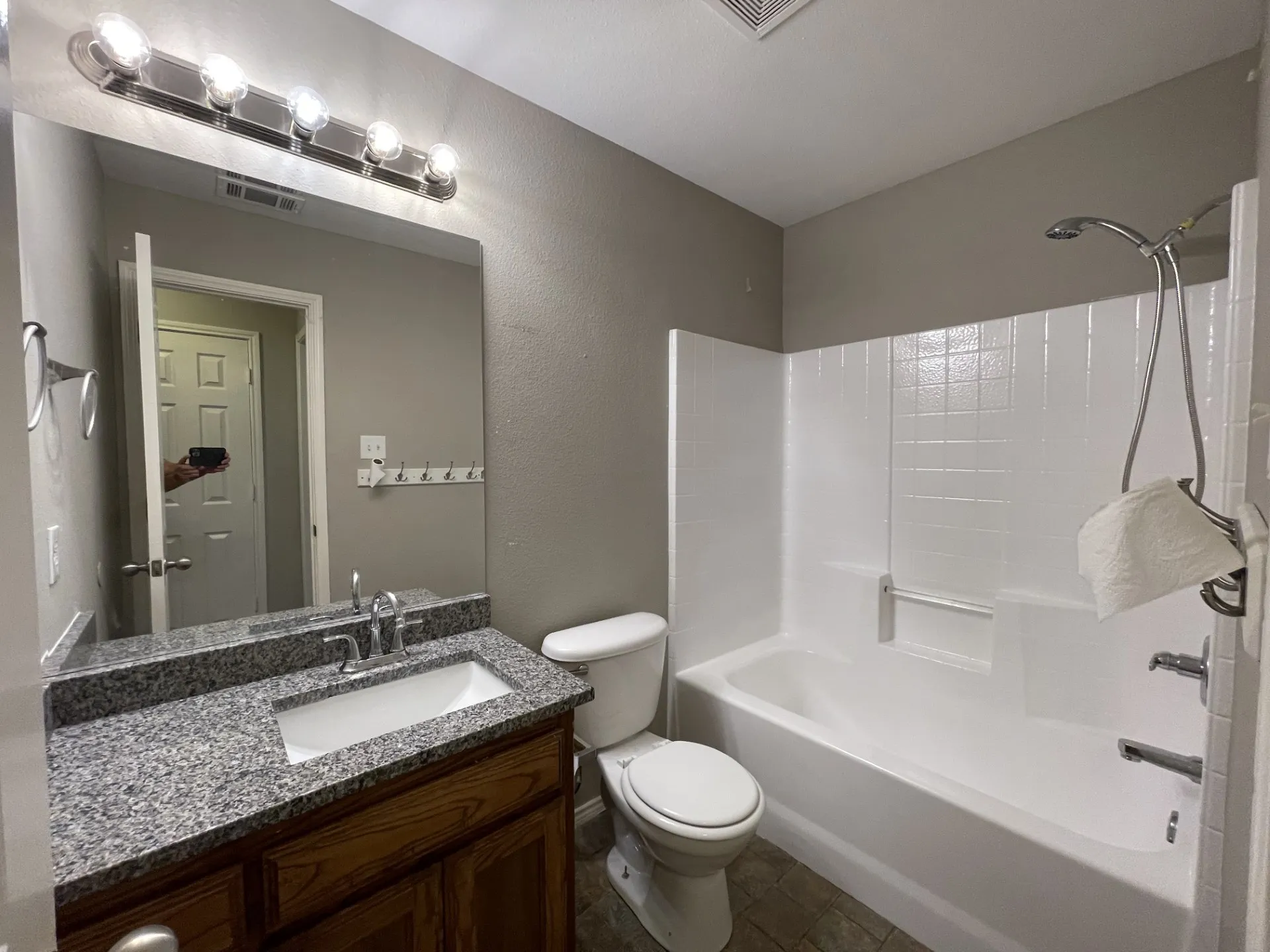 Full bathroom featuring a granite-style countertop vanity with a wood-finish base, a white drop-in sink, and a chrome faucet