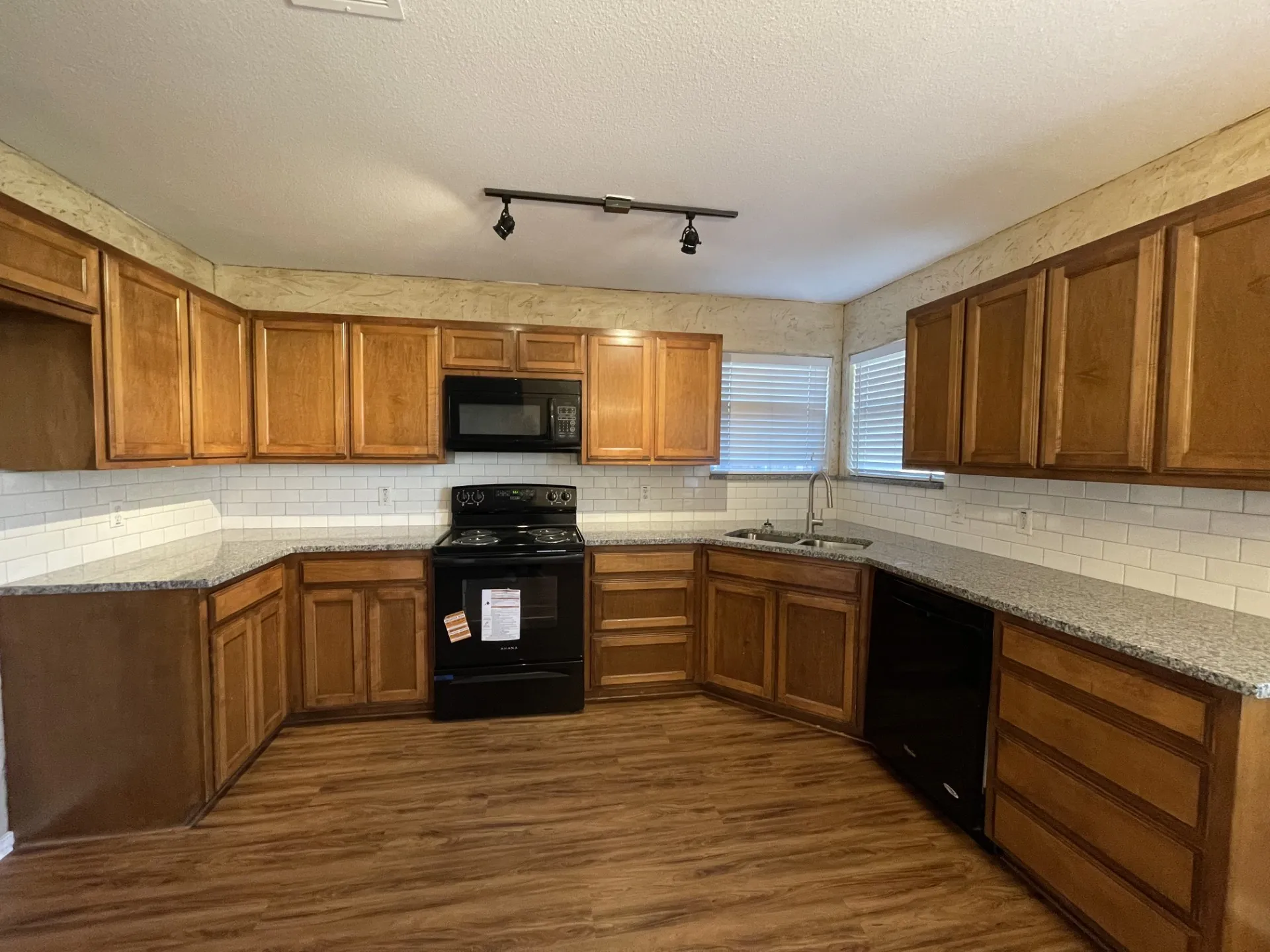 Kitchen featuring wood-finish cabinetry, granite-style countertops, subway tile backsplash, and wood-finish flooring