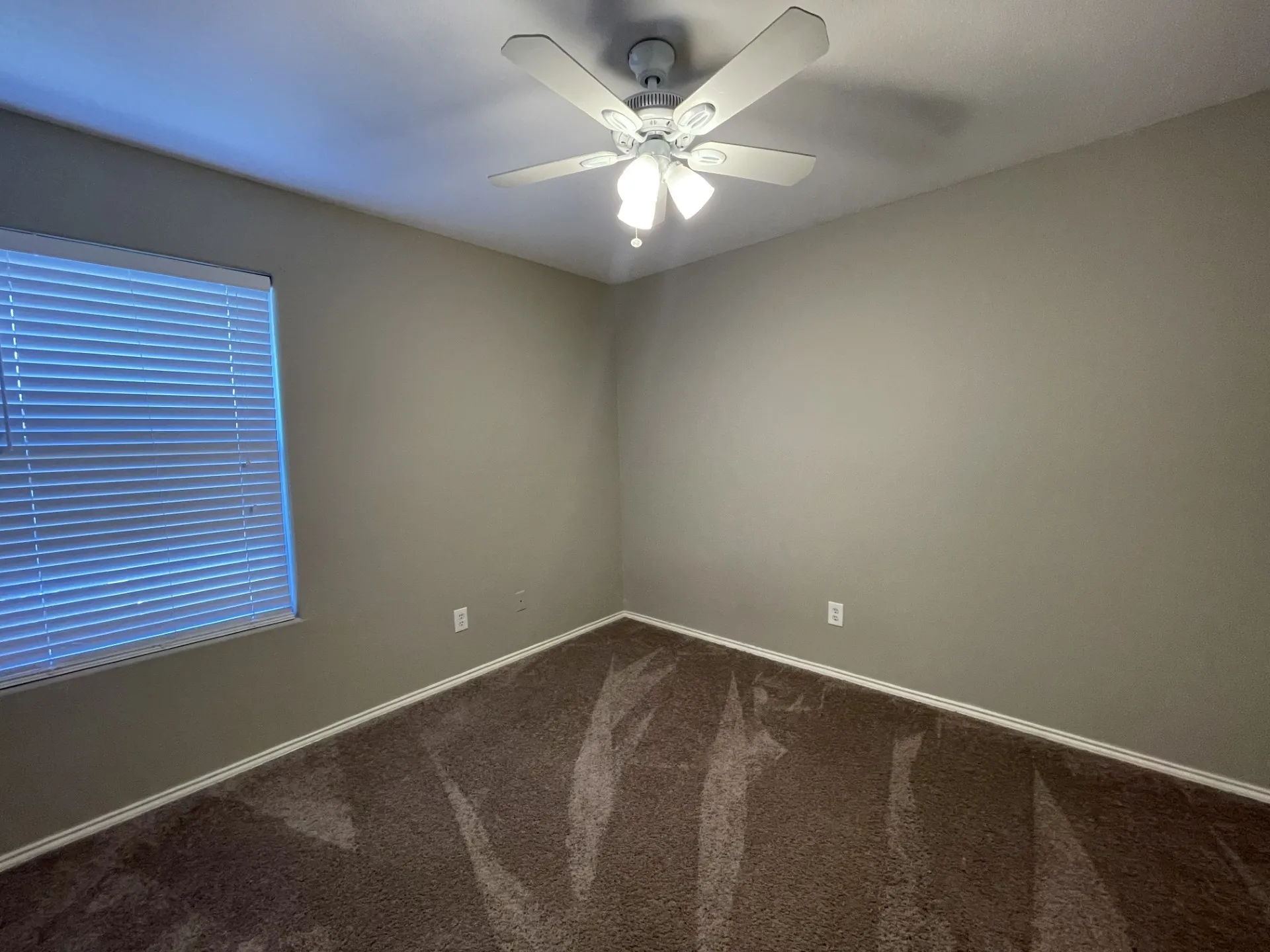 Room featuring neutral-toned walls, brown carpeting, and a ceiling fan with integrated lighting