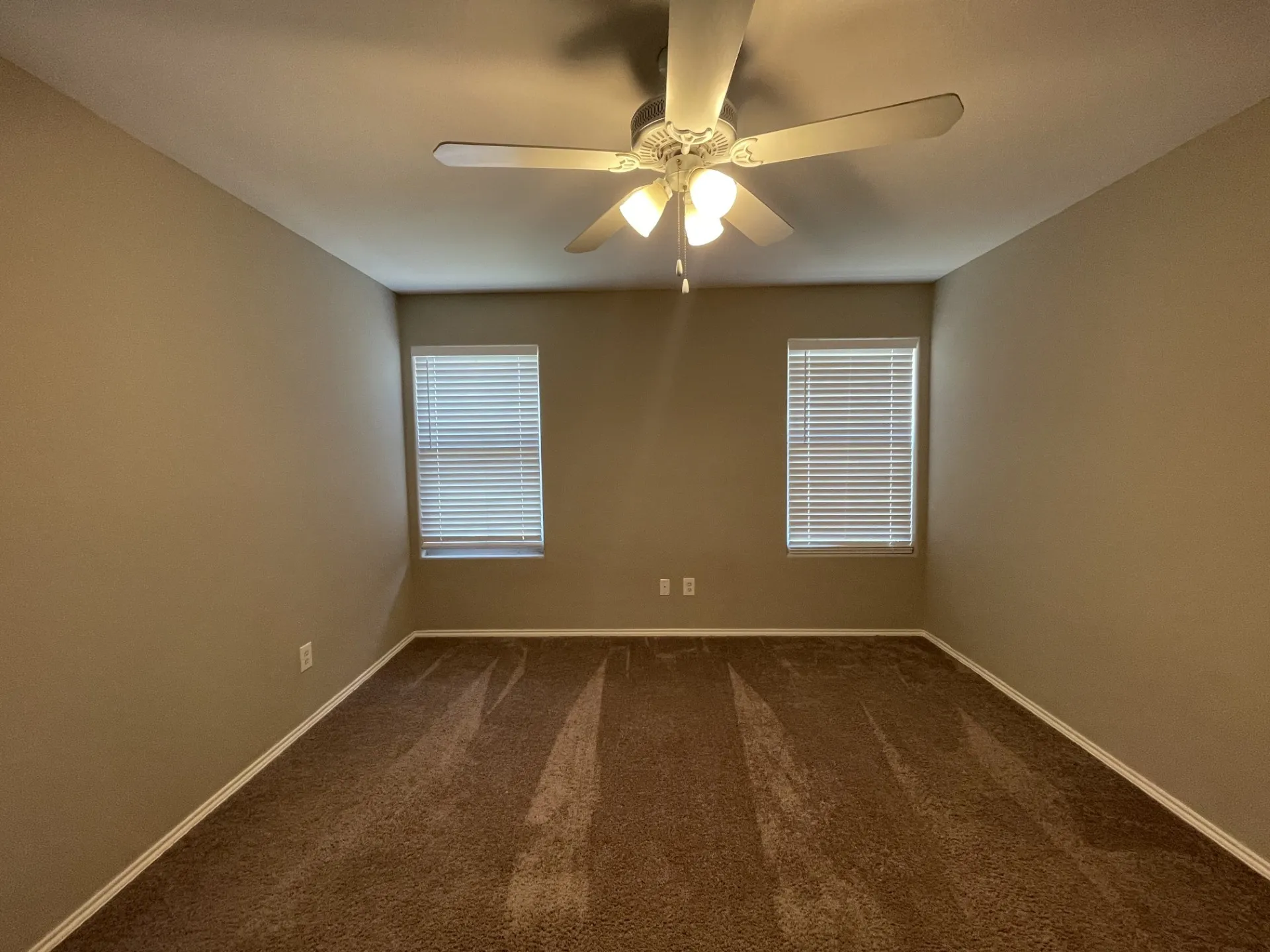 Carpeted room featuring dual windows with blinds, a ceiling fan with light fixture, and neutral painted walls