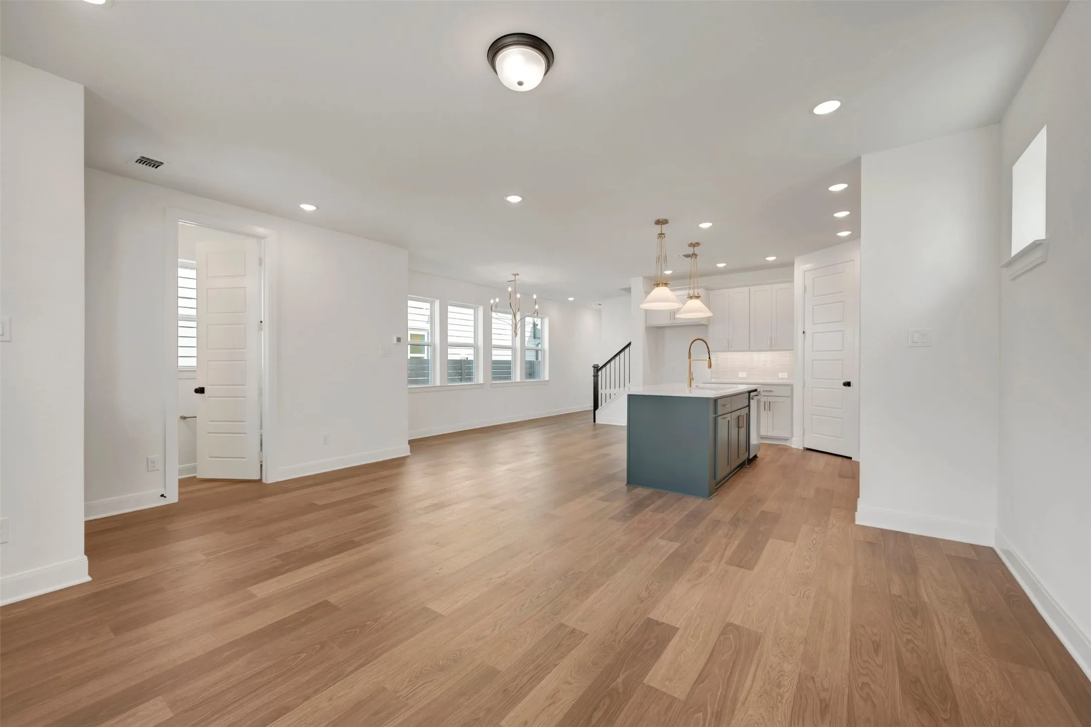 Expansive living area with wood-finish flooring, recessed lighting, and a modern kitchen island with pendant lighting