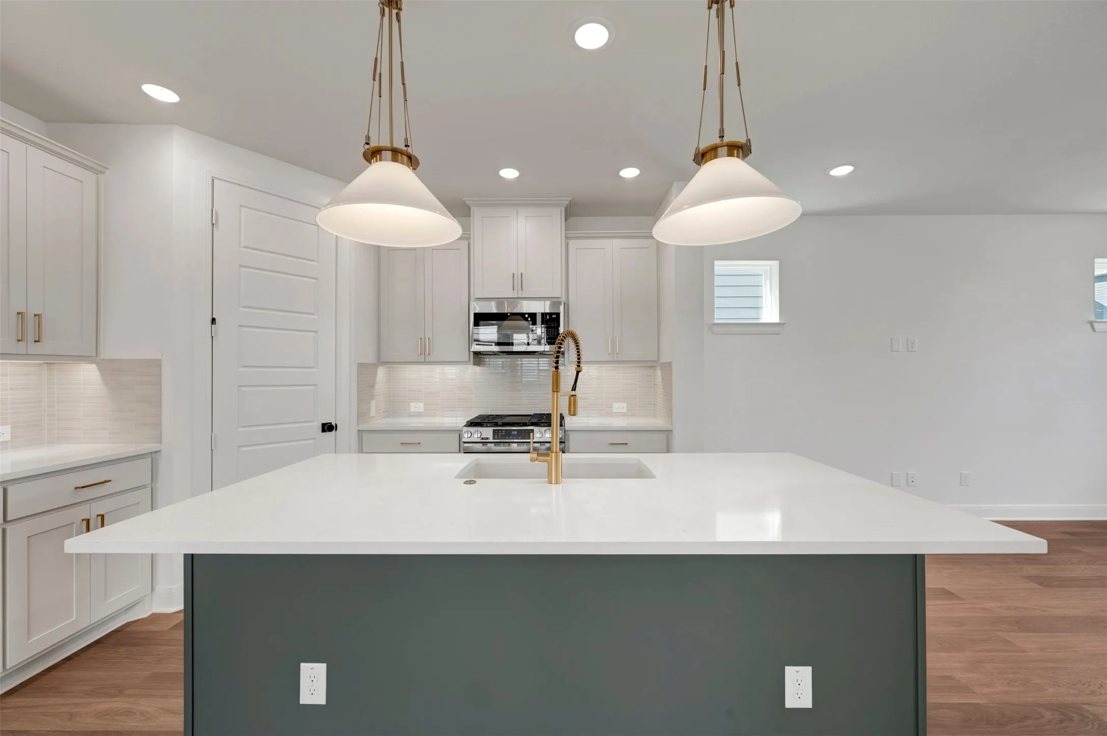 Kitchen featuring a large island with white countertop, pendant lighting, stainless steel appliances, and wood-finish flooring