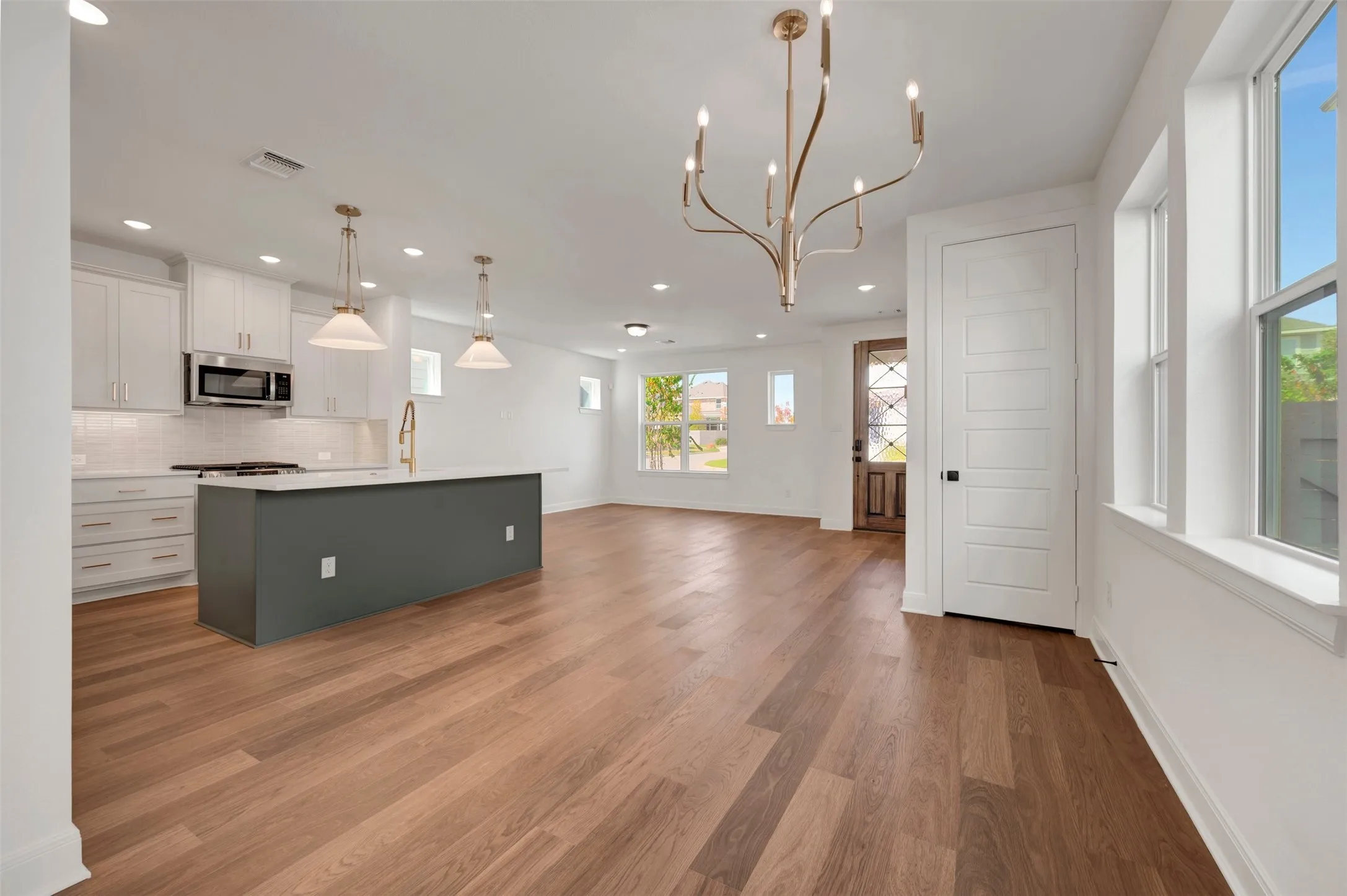 Open-concept living space with wood-finish flooring, a kitchen island featuring a gold-finish faucet, recessed lighting, and large windows