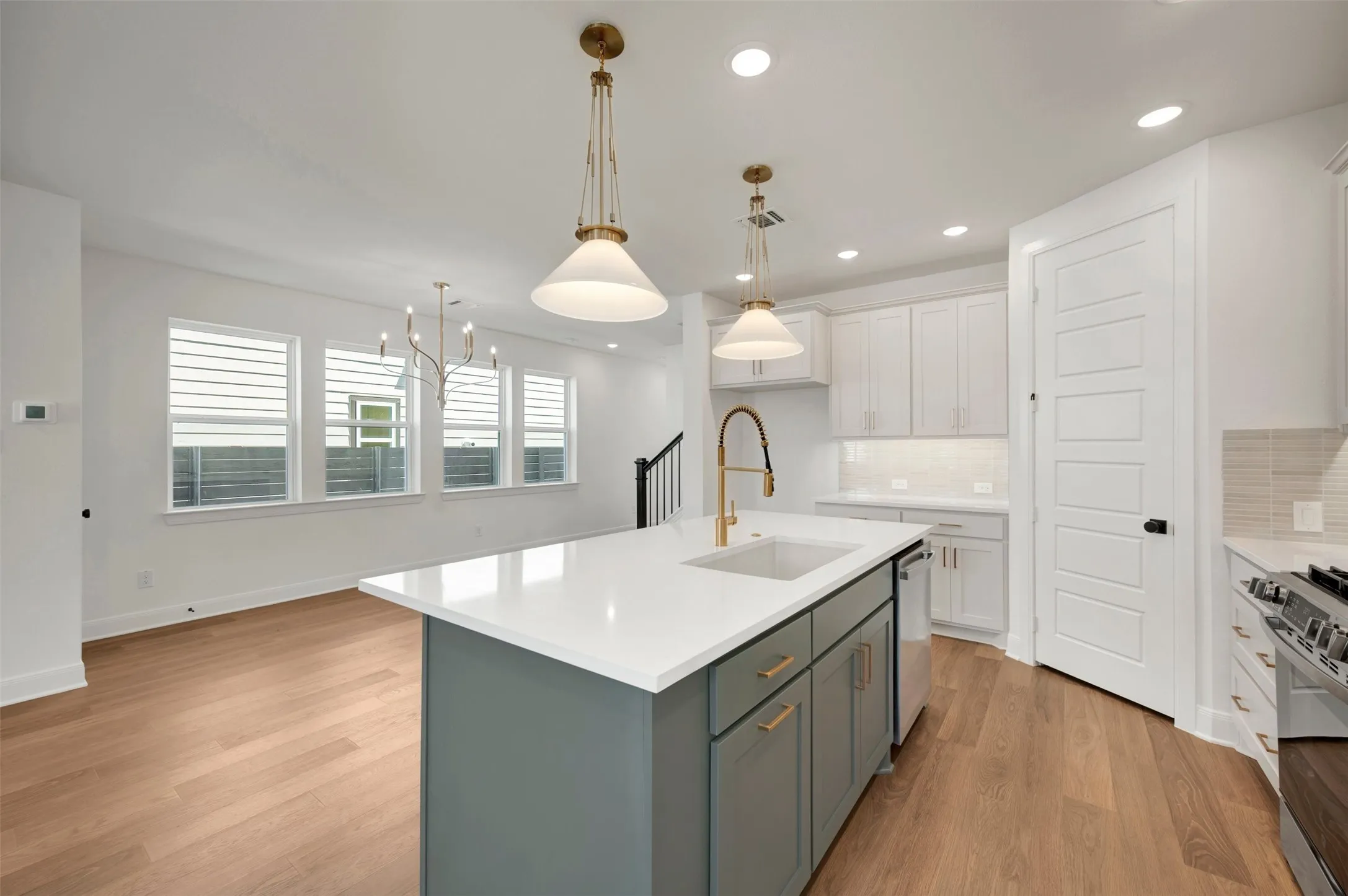 Kitchen island with integrated sink, white shaker cabinetry, wood-finish flooring, and recessed lighting