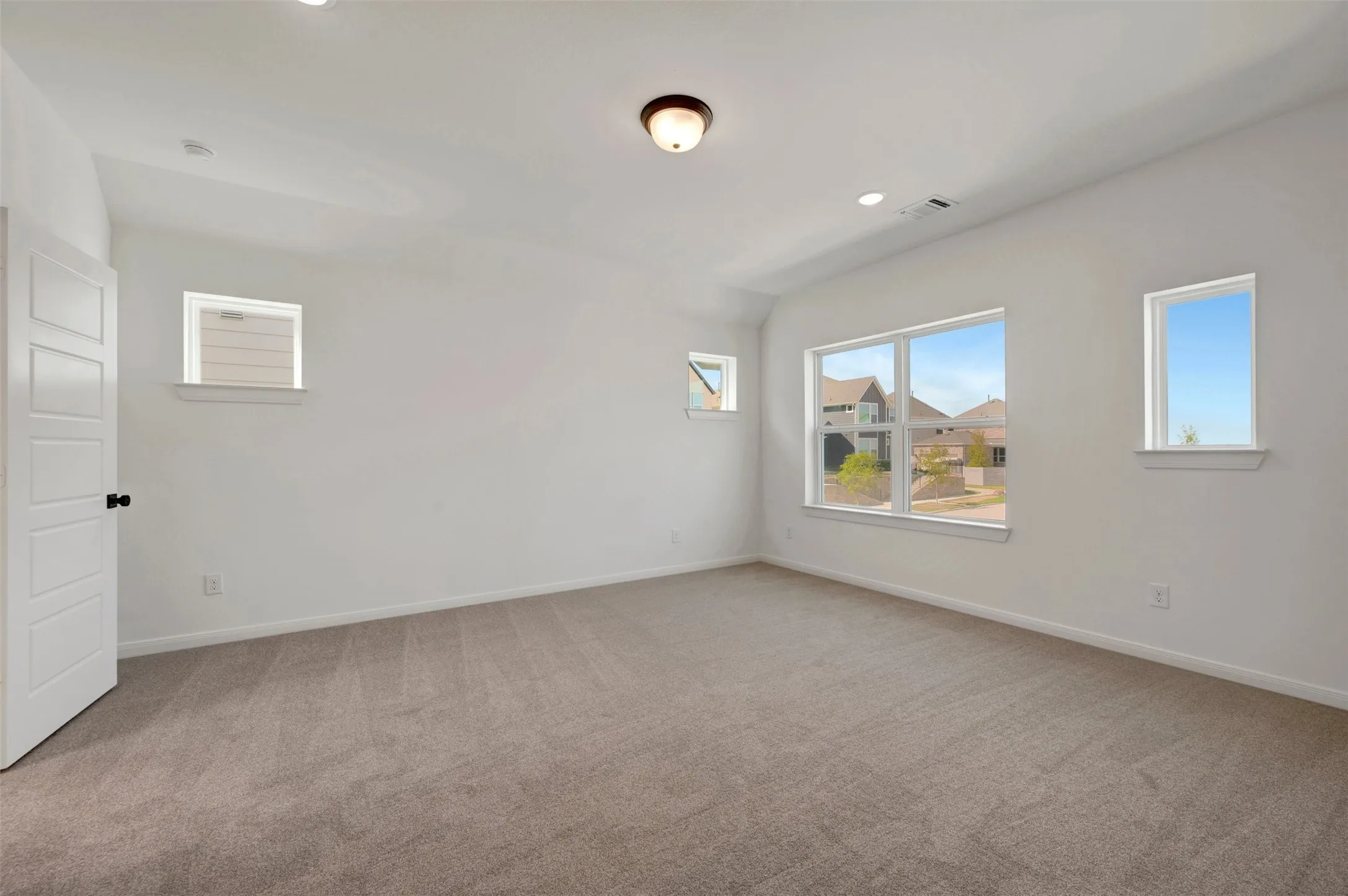 Spacious room featuring carpet flooring, multiple windows, a ceiling-mounted light fixture, and recessed lighting