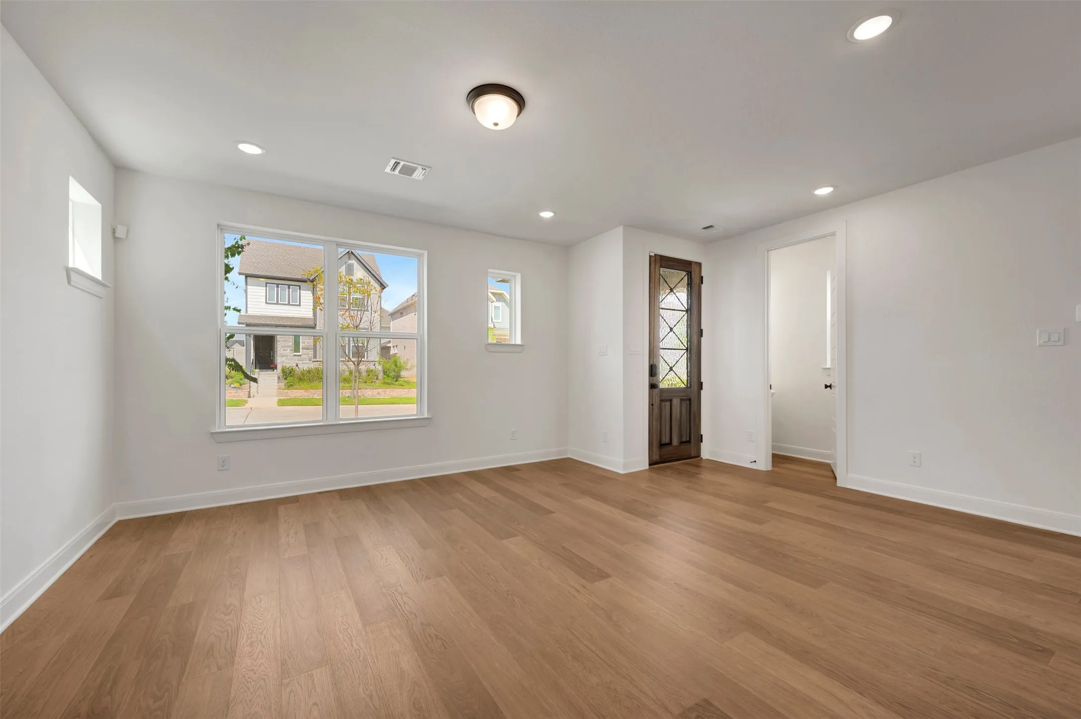 Wood-finish flooring, recessed lighting, white trim, and a dark wood entry door with glass panels