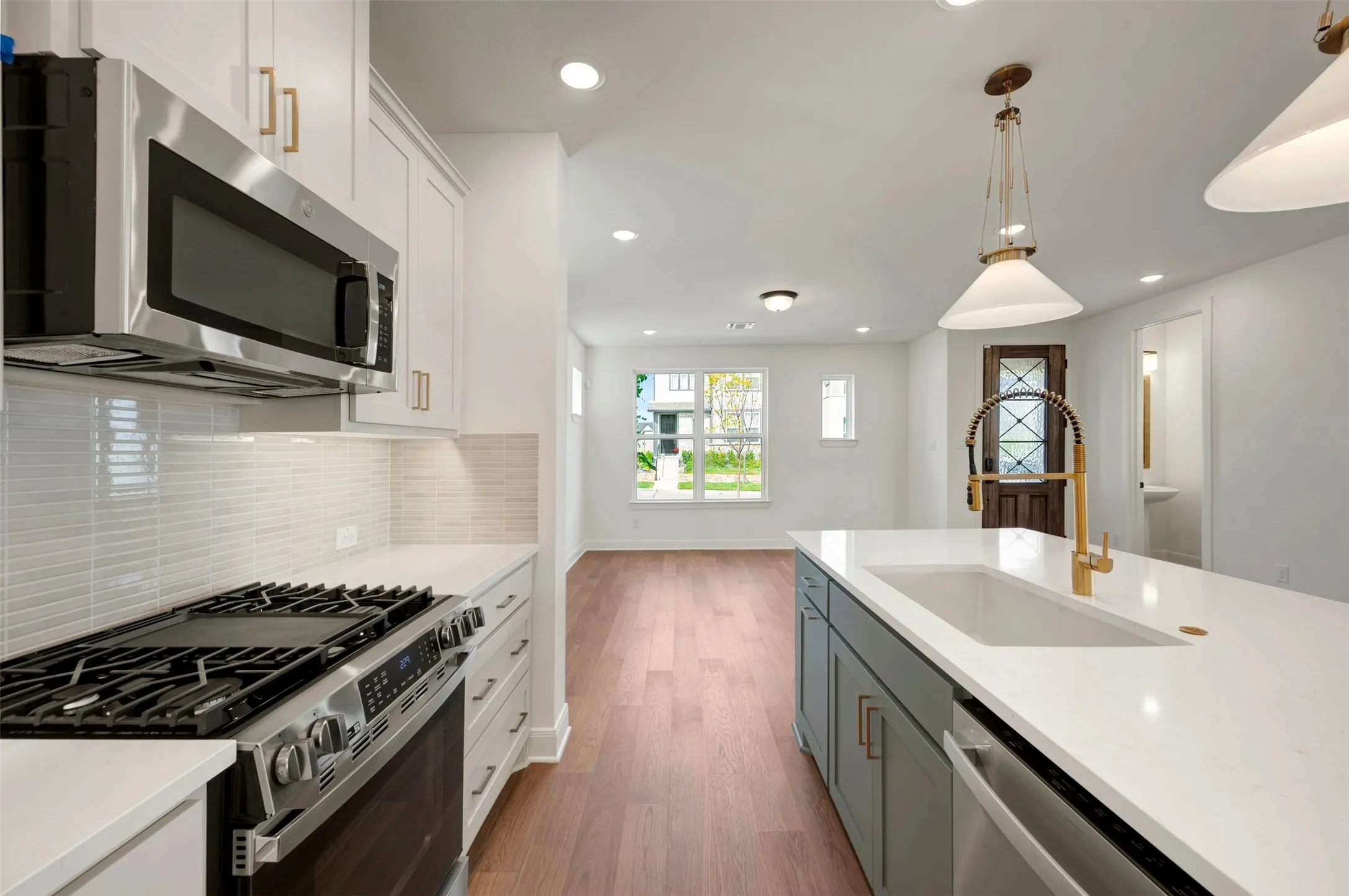 Kitchen featuring white cabinetry, stainless steel appliances, white subway tile backsplash, and a central island with a sink and pendant lighting