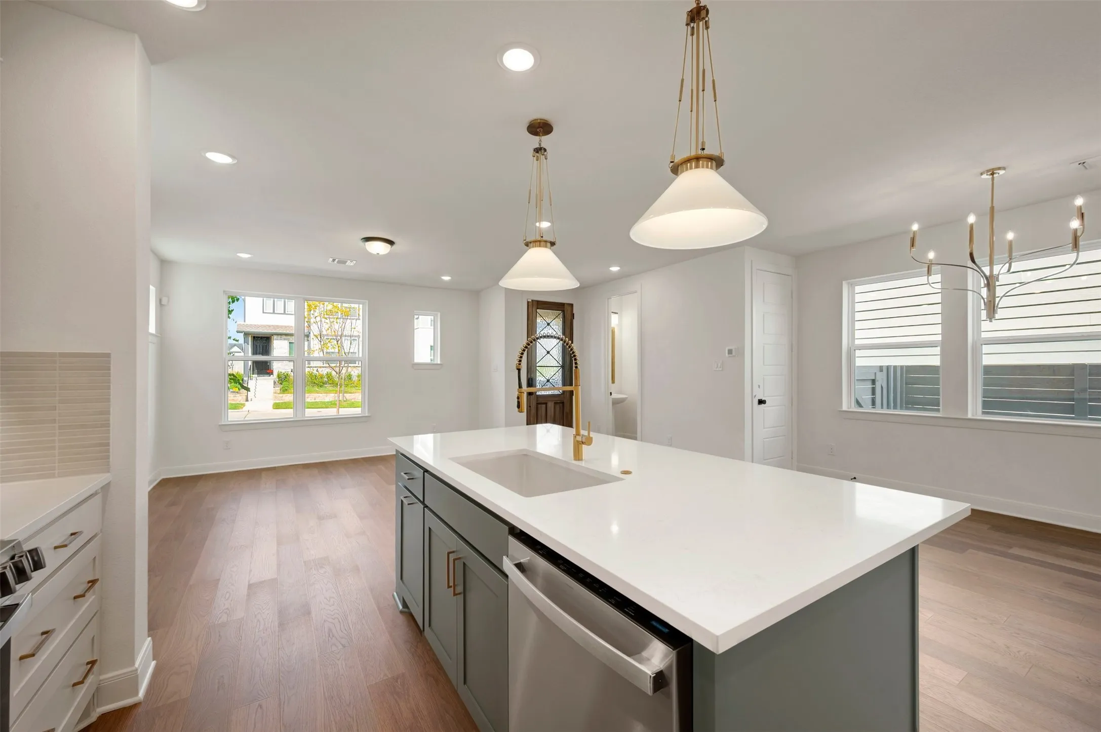 Kitchen island with a white countertop and integrated sink, stainless steel dishwasher, wood-finish flooring, and recessed lighting