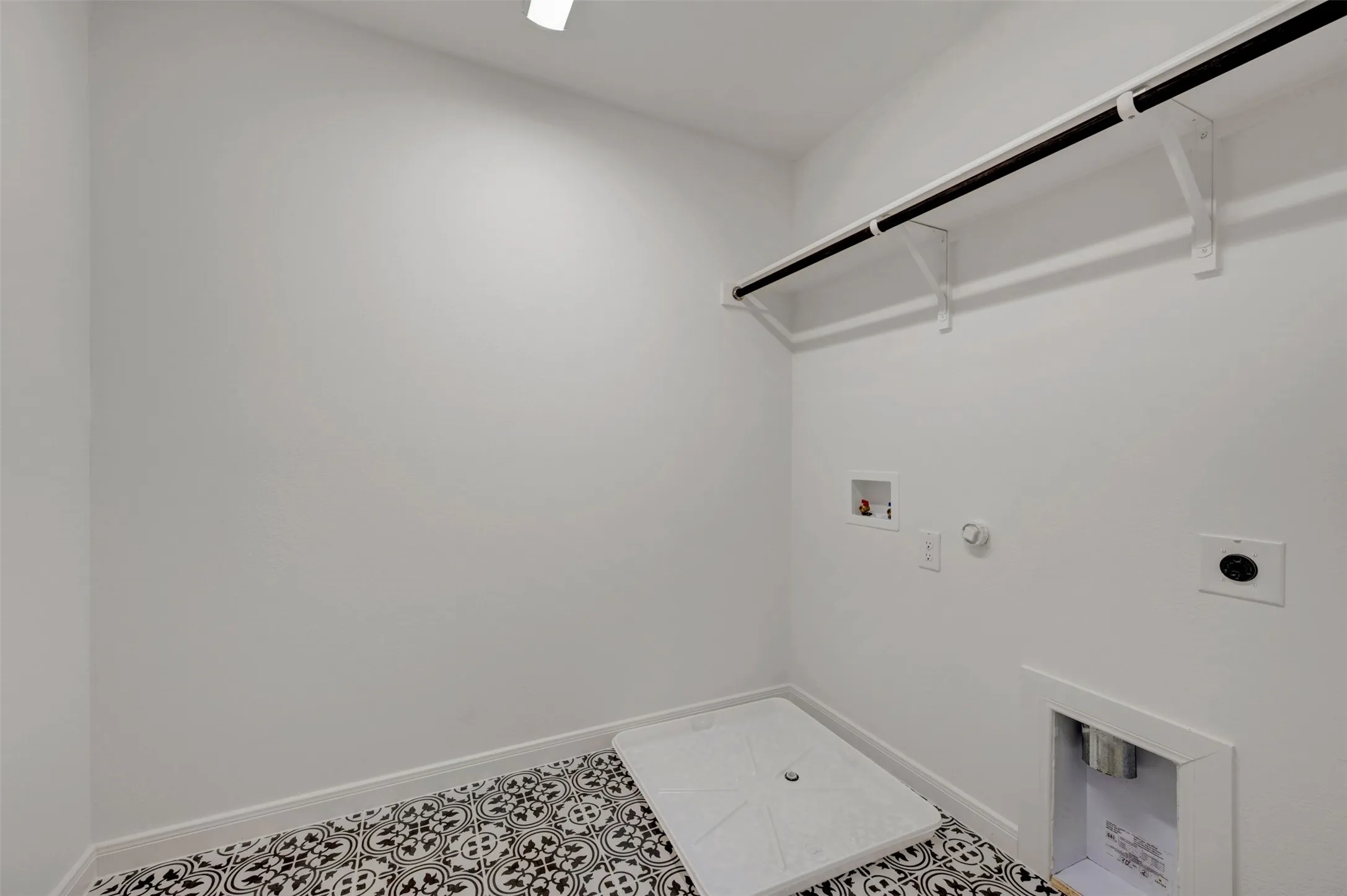 Laundry area featuring patterned floor tiles, white walls, and a built-in hanging rod