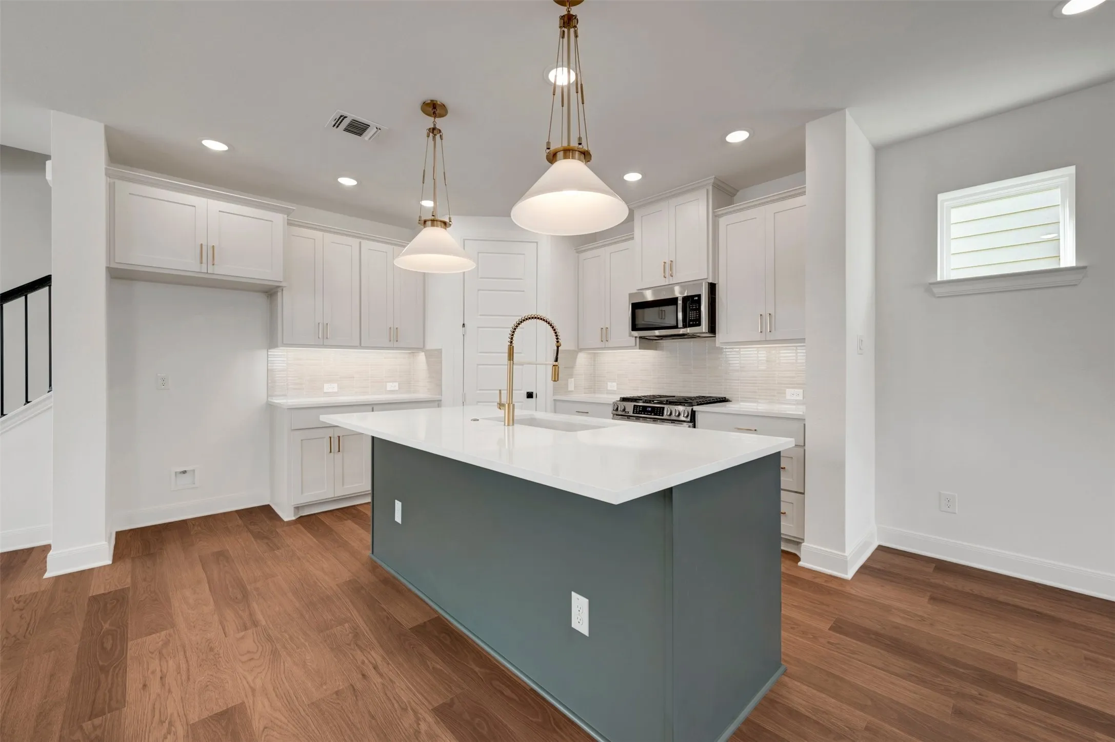 Kitchen featuring a center island with a white countertop, two pendant lights, wood-finish flooring, white cabinetry, and stainless steel appliances